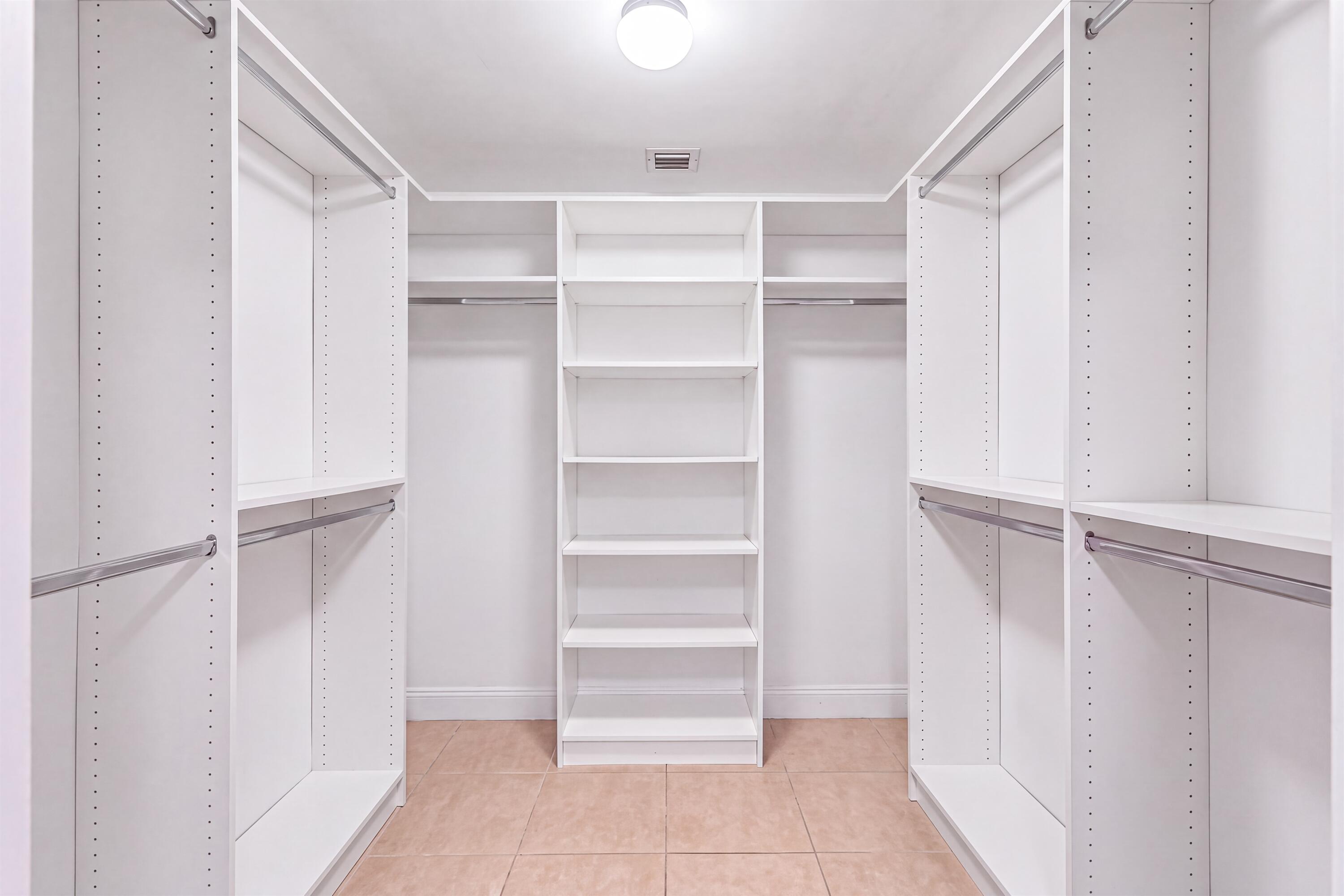 Walk-in closet featuring white built-in shelving, multiple hanging rods, and tile flooring