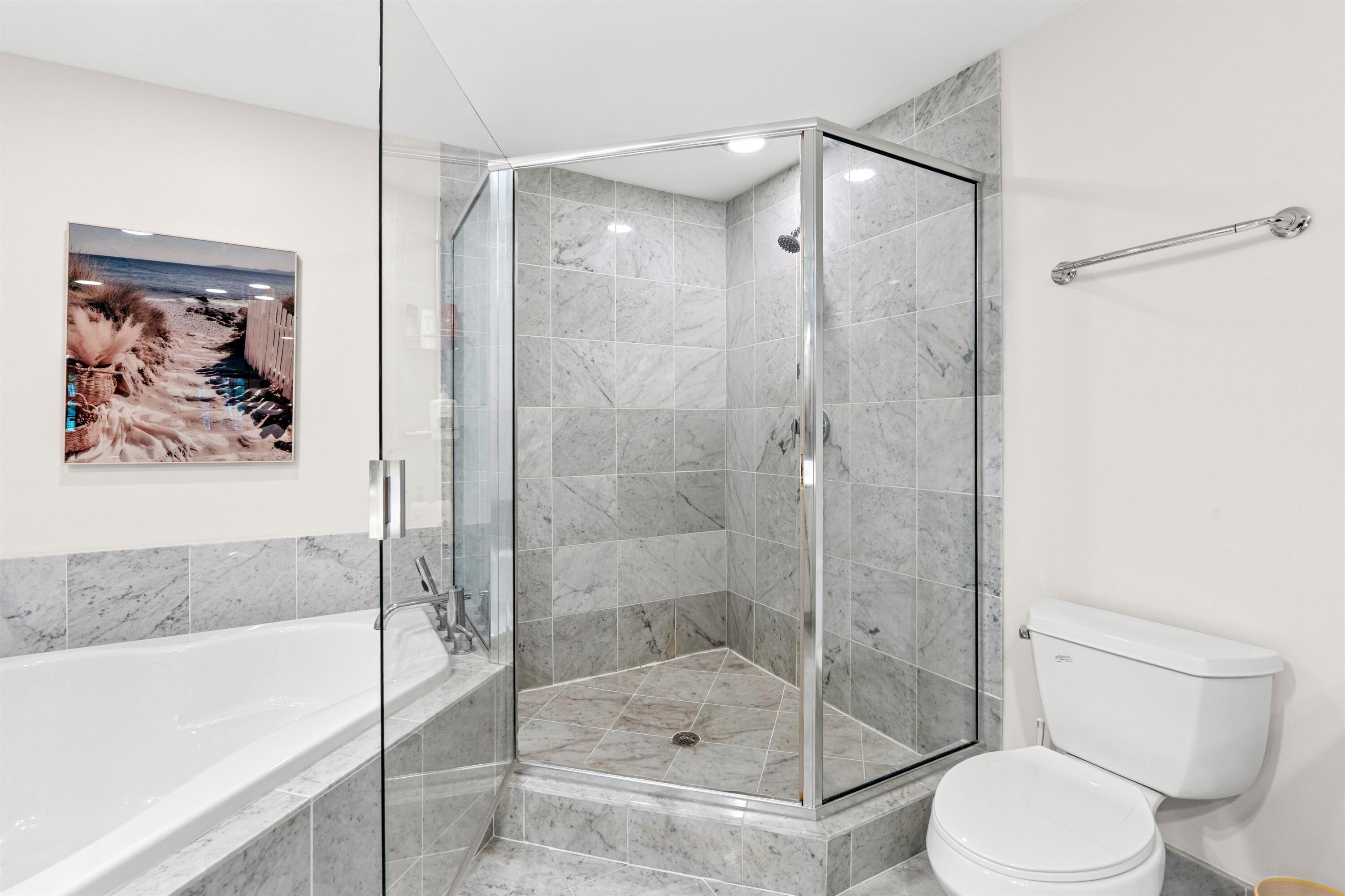 Corner shower enclosure featuring full-height stone tile surround, chrome-finish hardware, glass door, and soaking tub with stone tile deck