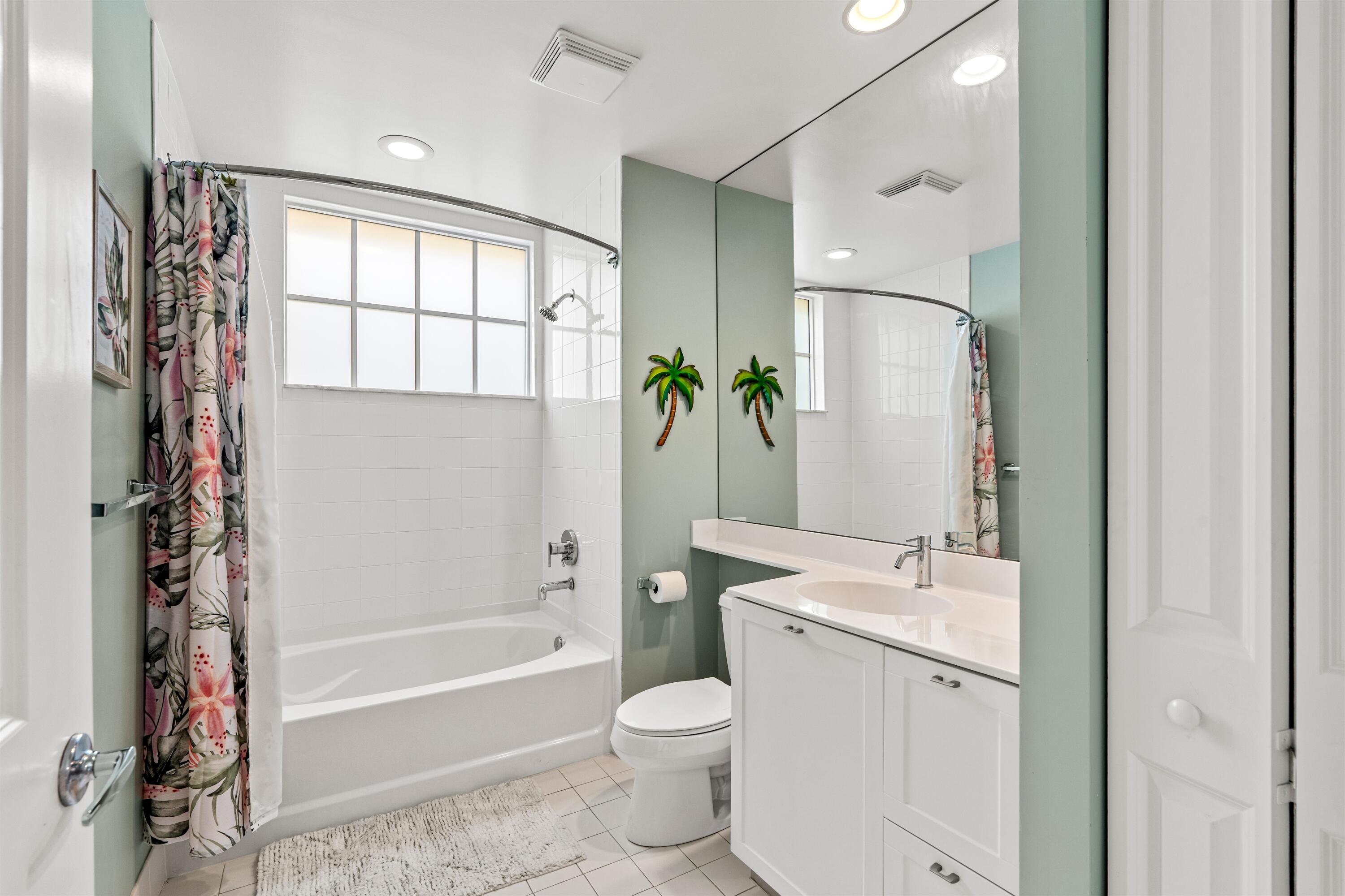 Bathroom featuring a white vanity cabinet with an integrated sink, full-width wall mirror, tub and shower combination with tile surround, grid-patterned window, and recessed lighting