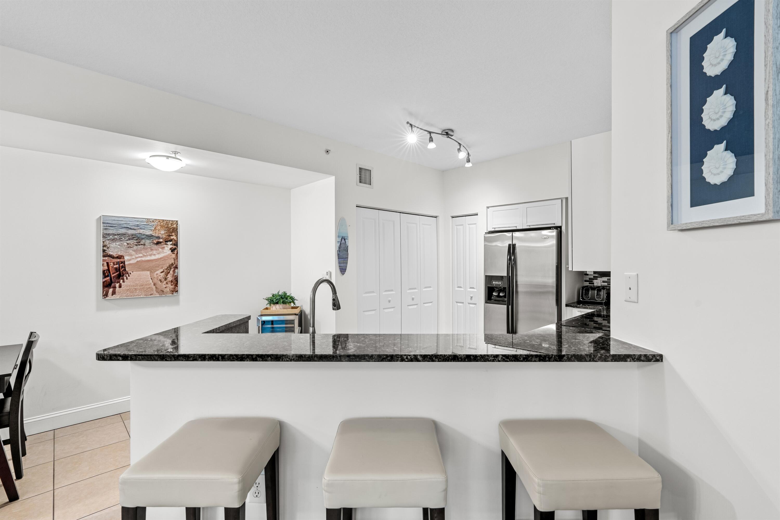 Kitchen featuring stone countertops, breakfast bar with integrated sink, stainless steel refrigerator, white cabinetry, and multi-directional track lighting