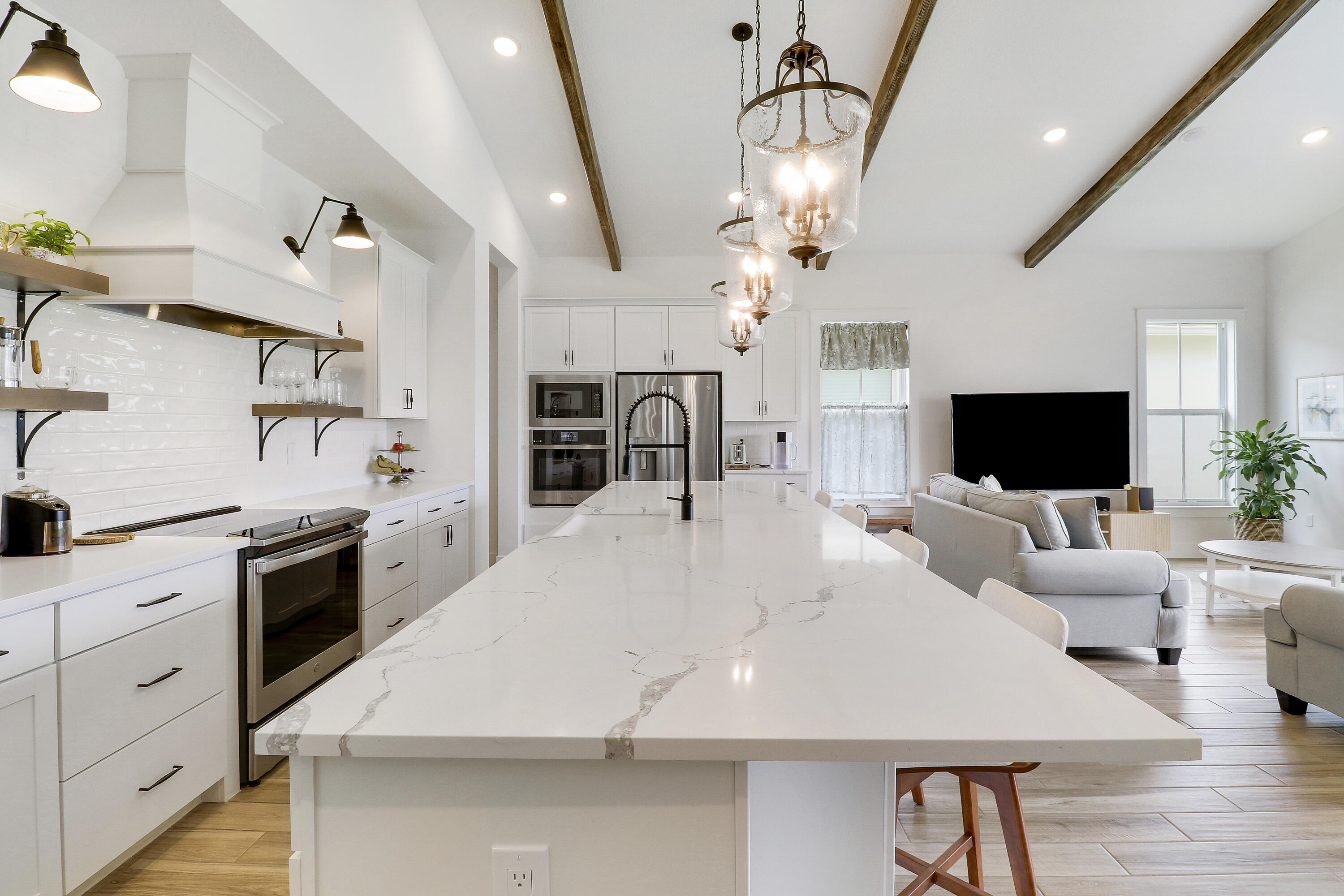 Kitchen featuring a central island with a stone countertop, white shaker cabinetry, stainless steel built-in appliances, decorative ceiling beams, and tile wood like flooring