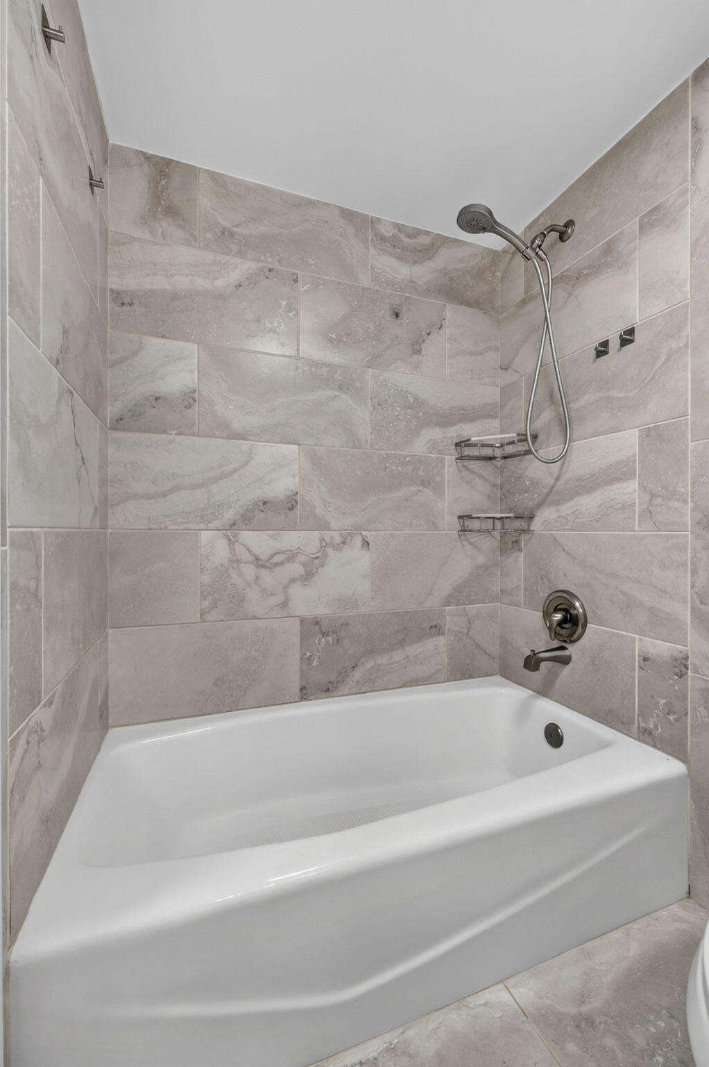 Bathtub and shower combination featuring large-format ceramic tile surround, integrated metal corner shelving, and oil-rubbed bronze plumbing fixtures