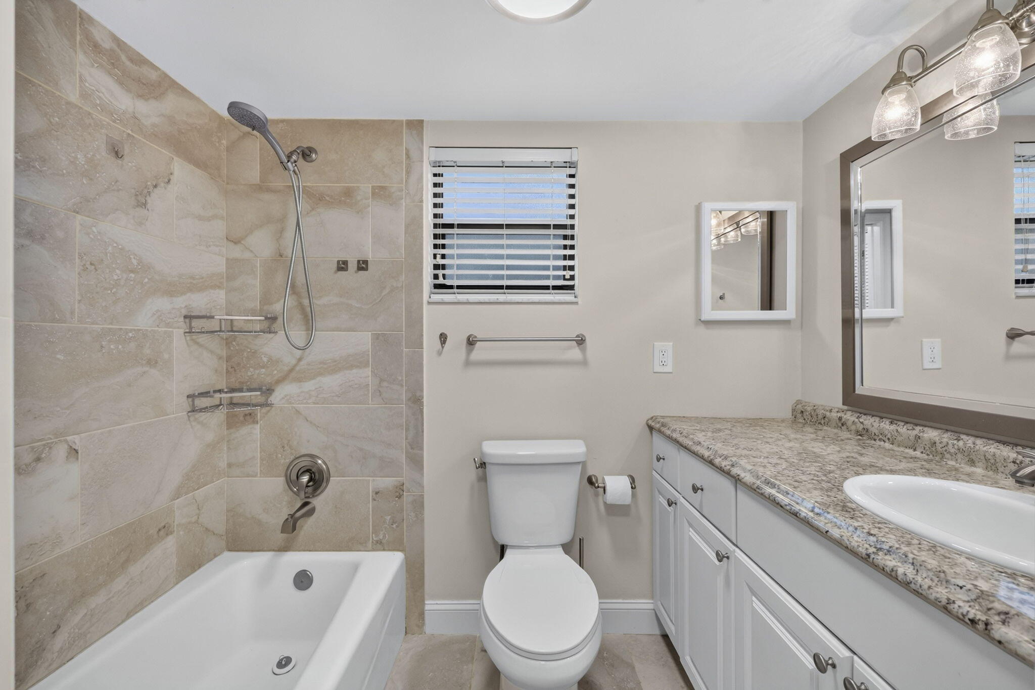 Bathroom featuring a tub-shower combination with floor-to-ceiling tile surround, vanity with stone-finish countertop, dual-light fixture, and recessed mirror