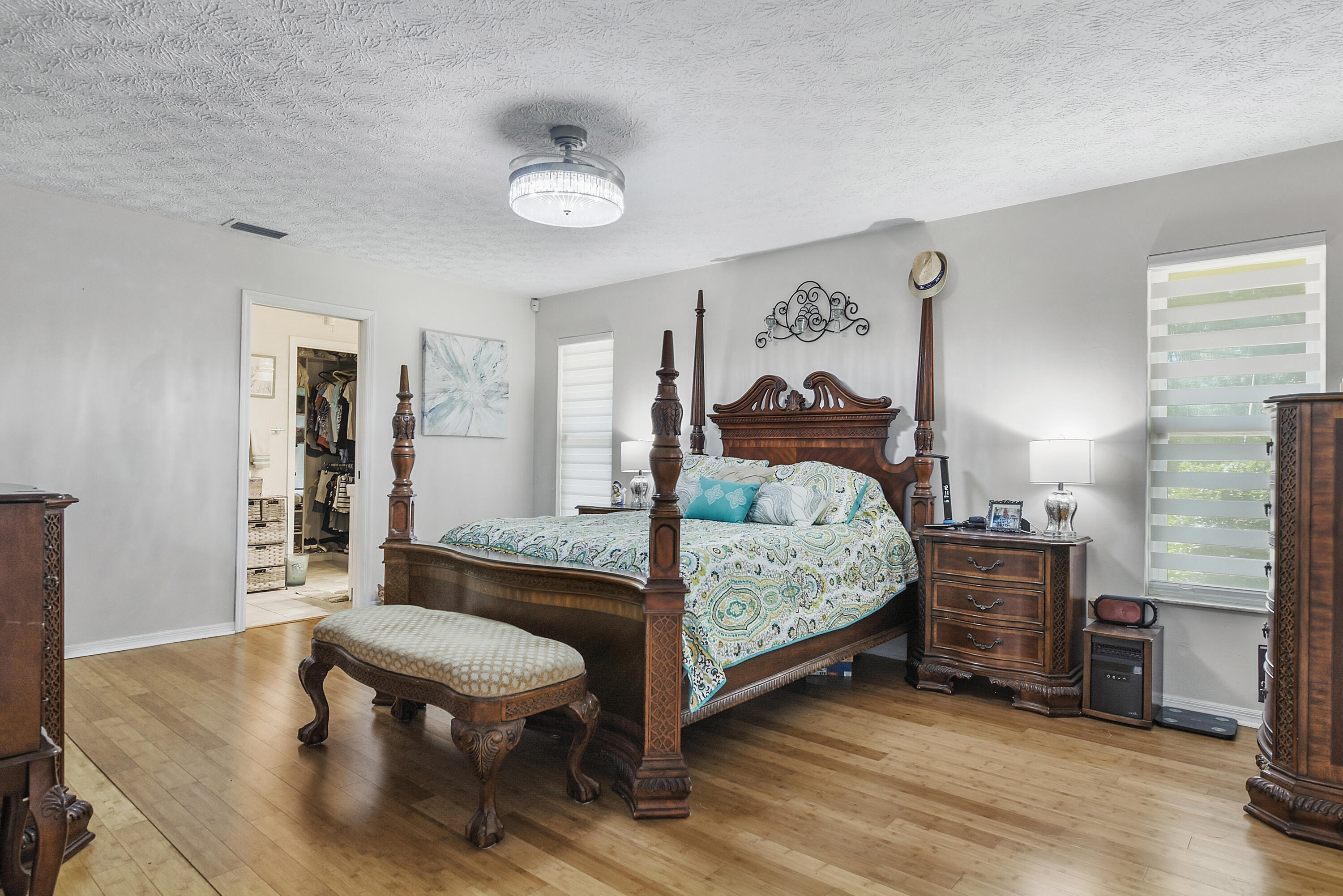Inviting primary suite featuring bamboo beautiful flooring, stylish window treatments, two walk-in closets, and a brand-new ceiling fan with lighting.