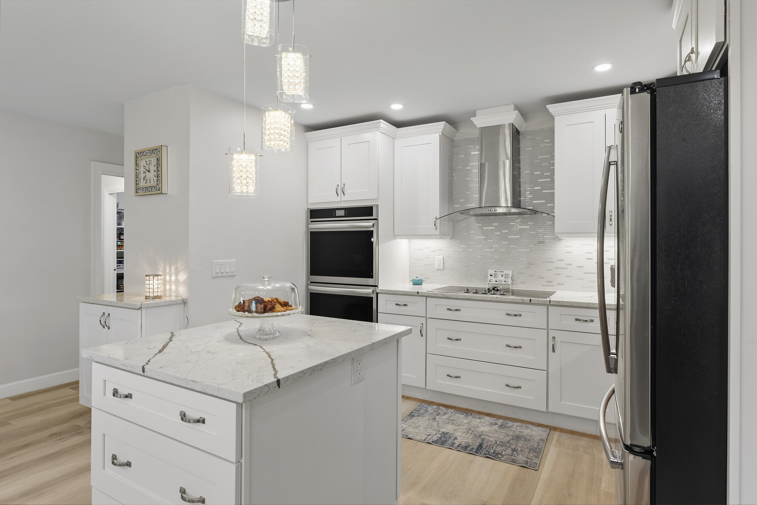 A beautifully designed chef's kitchen featuring a spacious prep island with dramatic marble-look countertops, high-end multifunction double ovens, sleek cooktop, decorative tile backsplash, and elegant pendant lighting. A dream kitchen for anyone who loves to cook!