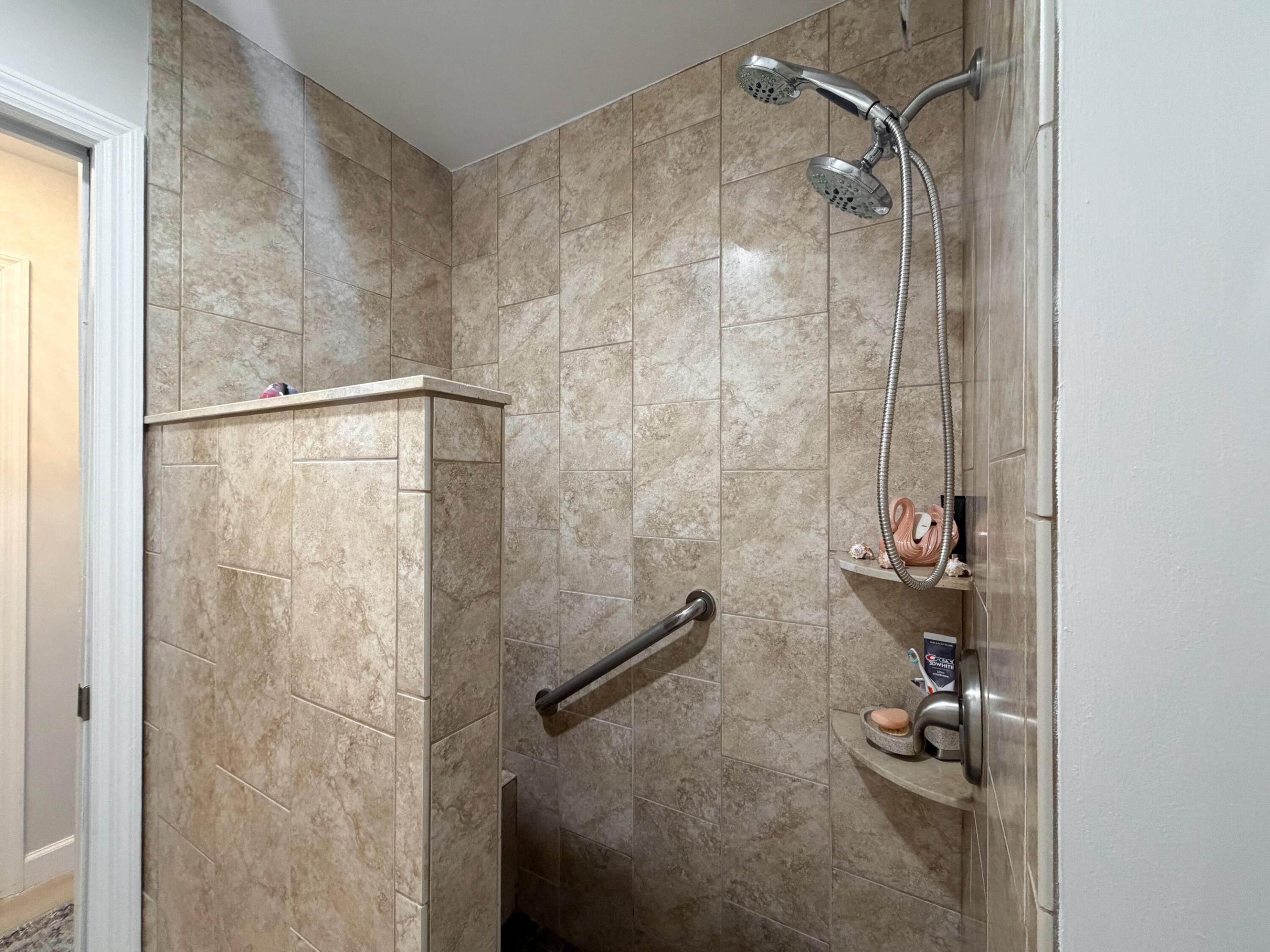 Enjoy a walk-in shower featuring floor-to-ceiling tile, a convenient built-in bench, handheld showerhead, and grab bar for added comfort.