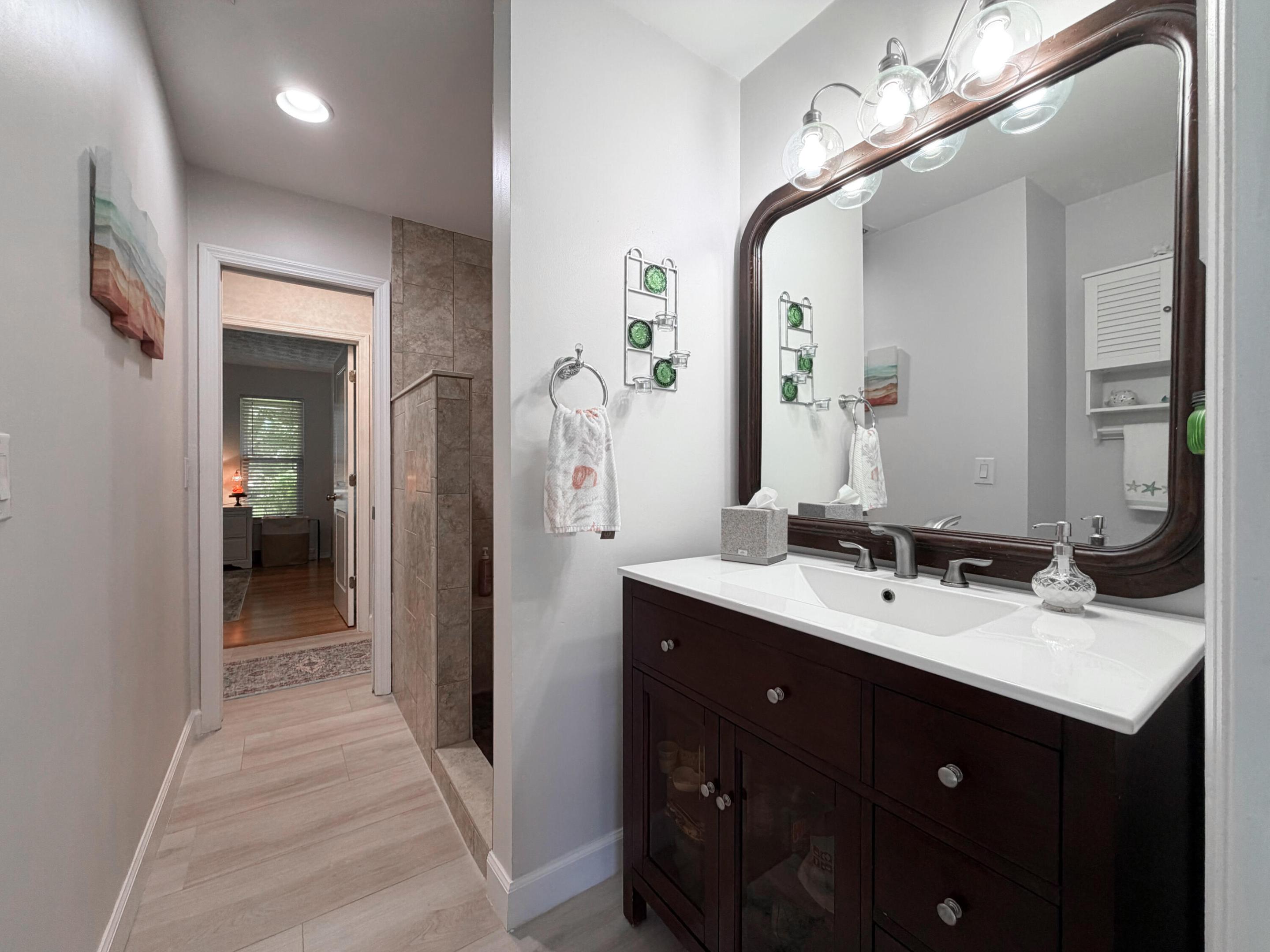 Featuring a rich wood vanity, modern lighting, and a tiled walk-in shower.
