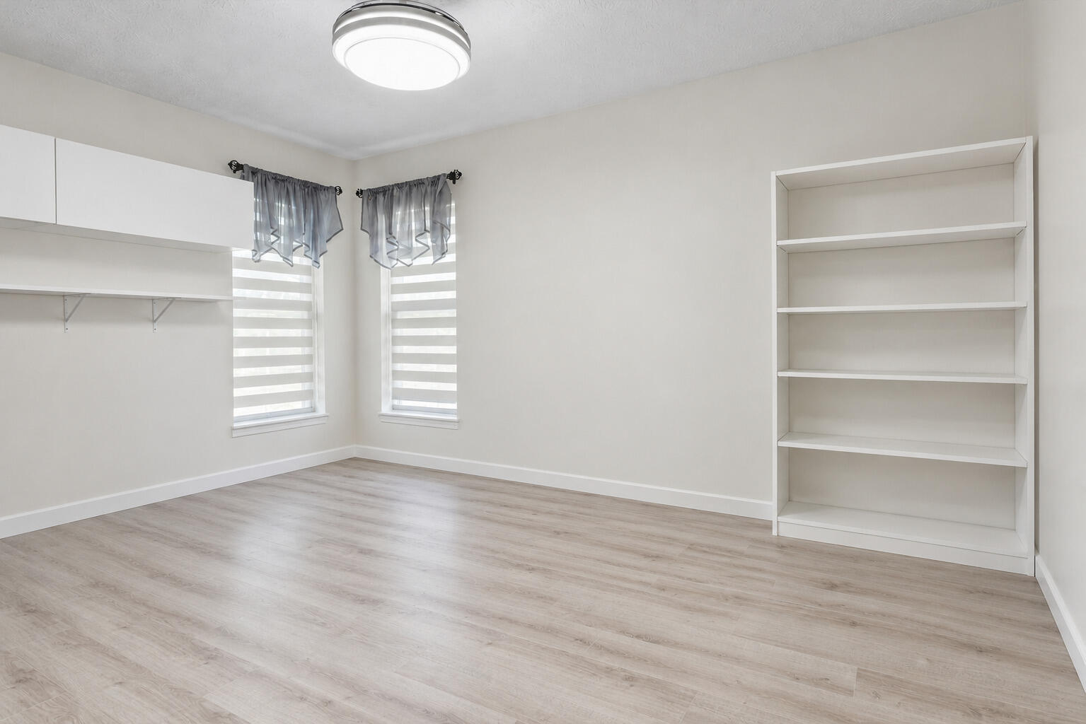 Bedroom 4 shown without furniture, highlighting beautiful flooring, built-in shelving, stylish window treatments, and flexibility for use as a bedroom, home office, or hobby room.