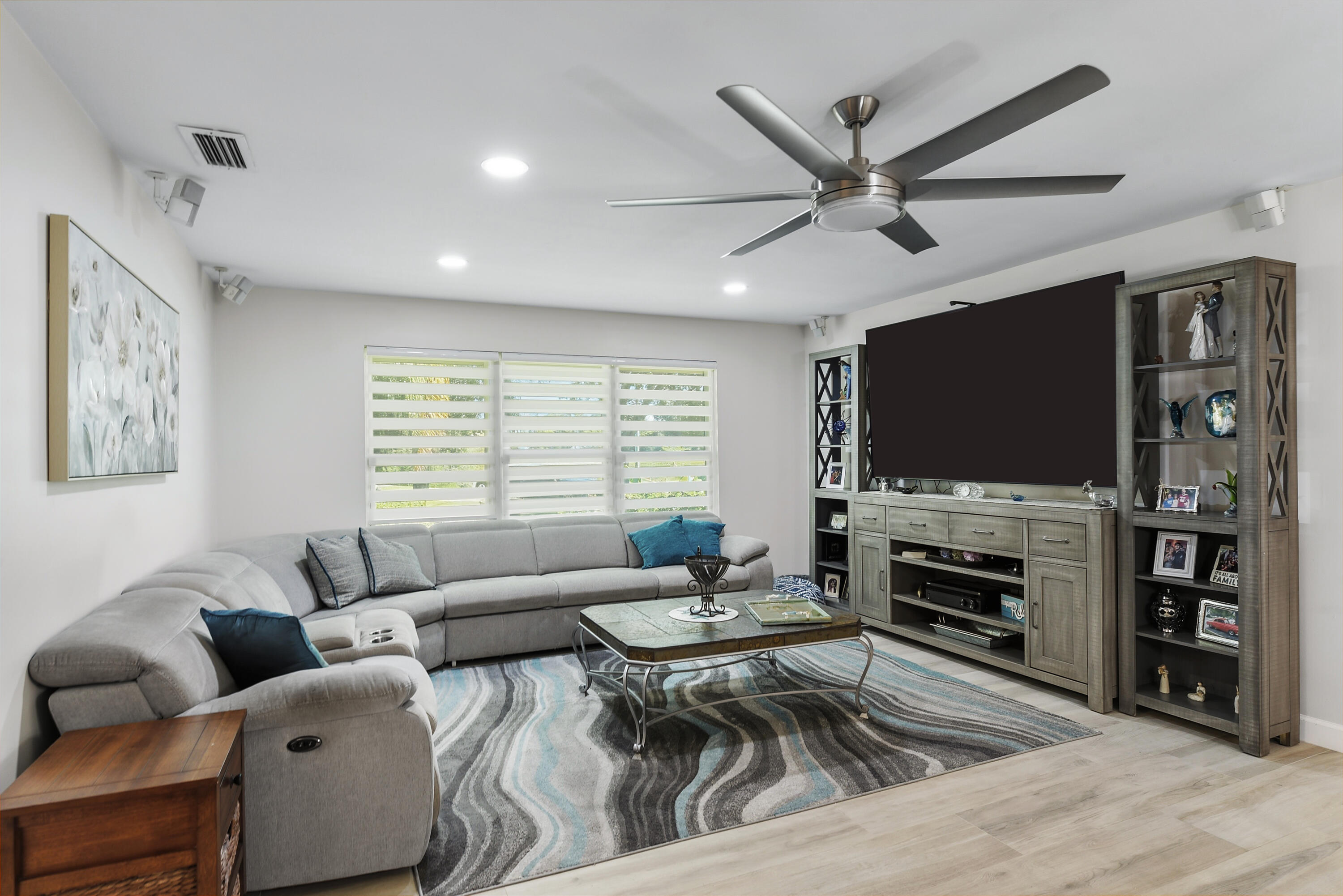A fantastic family room featuring beautiful wide-plank flooring, a large entertainment center, stylish ceiling fan, and abundant natural light. Plenty of space for movie nights, relaxing, and gathering with family and friends!