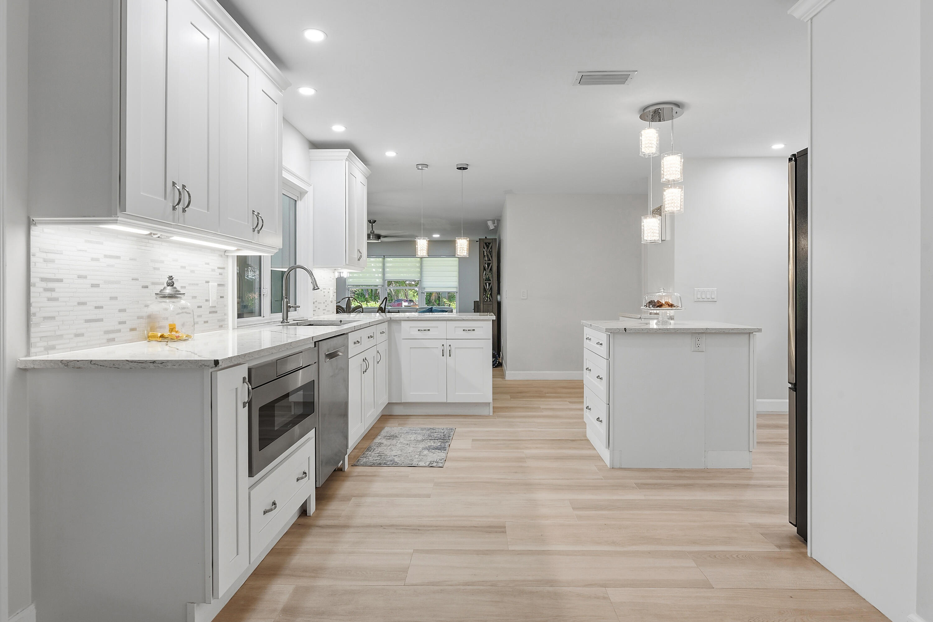 beautifully remodeled kitchen featuring abundant white cabinetry, marble-look countertops, stainless steel appliances, stylish pendant lighting, and a spacious prep island. A chef's dream!