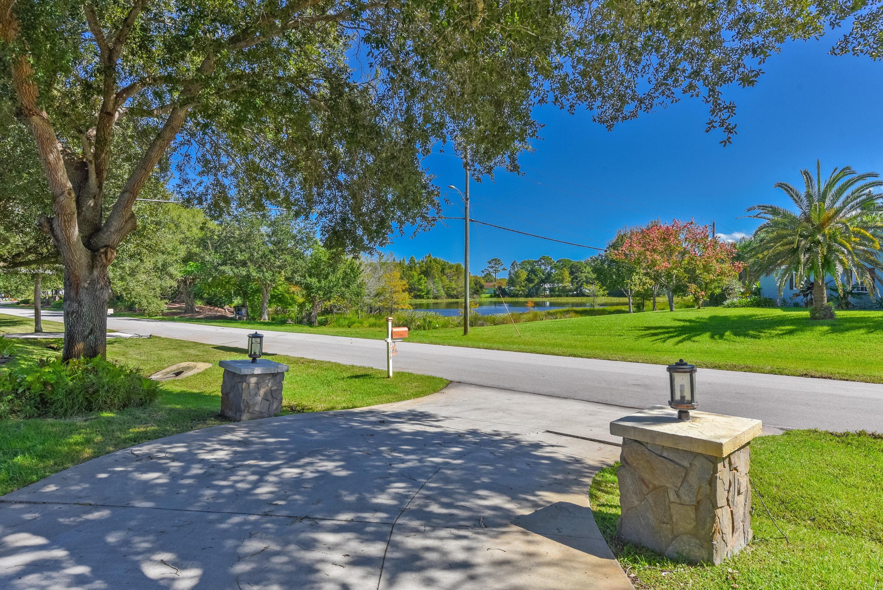 Enjoy a spacious driveway framed by decorative stone pillars, mature shade trees, lush landscaping