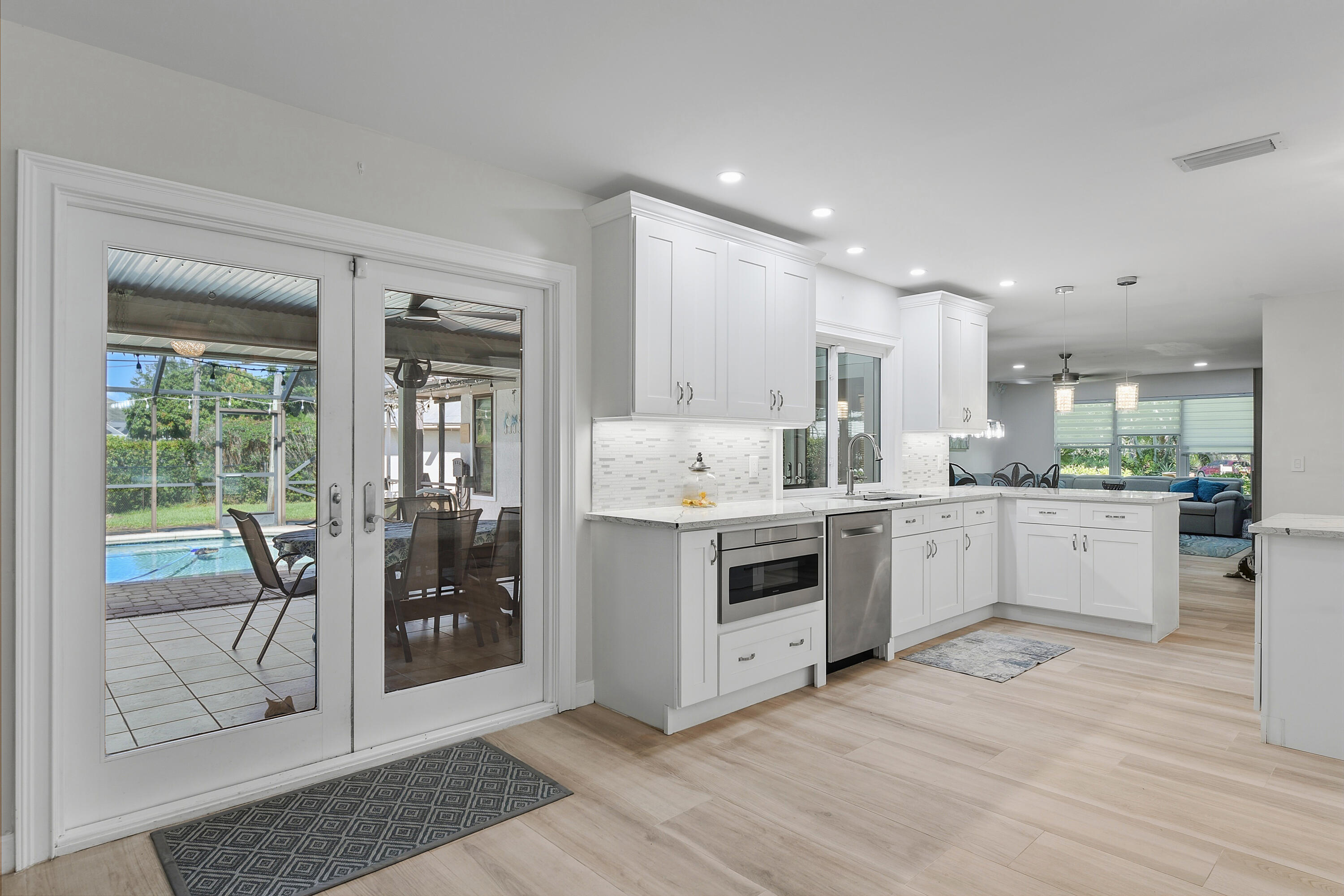 Beautifully remodeled kitchen with white cabinetry, marble-look countertops, and French doors leading to the spacious screened lanai and pool. Perfect for indoor-outdoor entertaining!