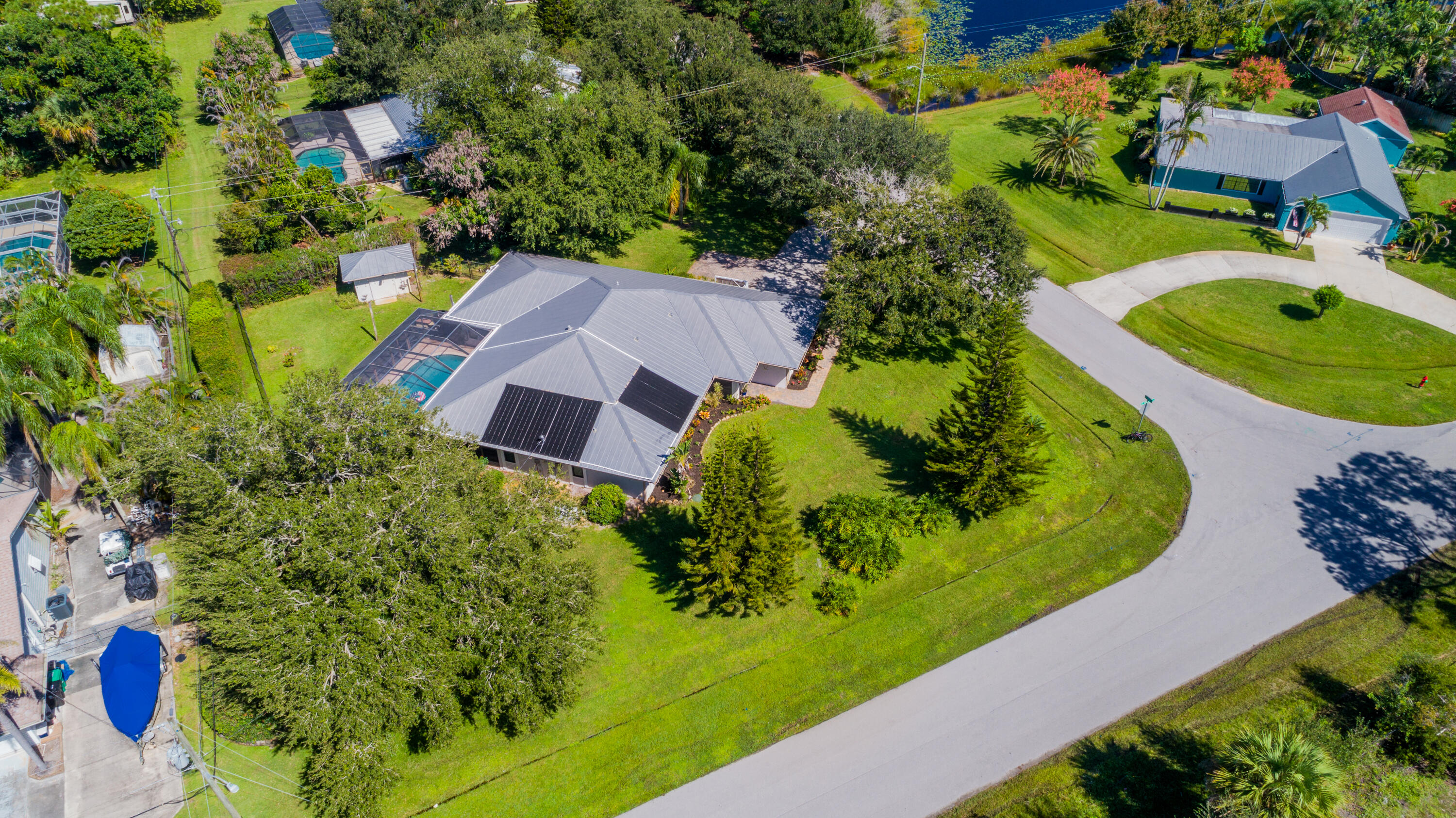 Aerial view showcasing the metal roof, beautifully landscaped .49-acre lot, screened pool, and additional paved parking ideal for your boat or recreational toys. No HOA!