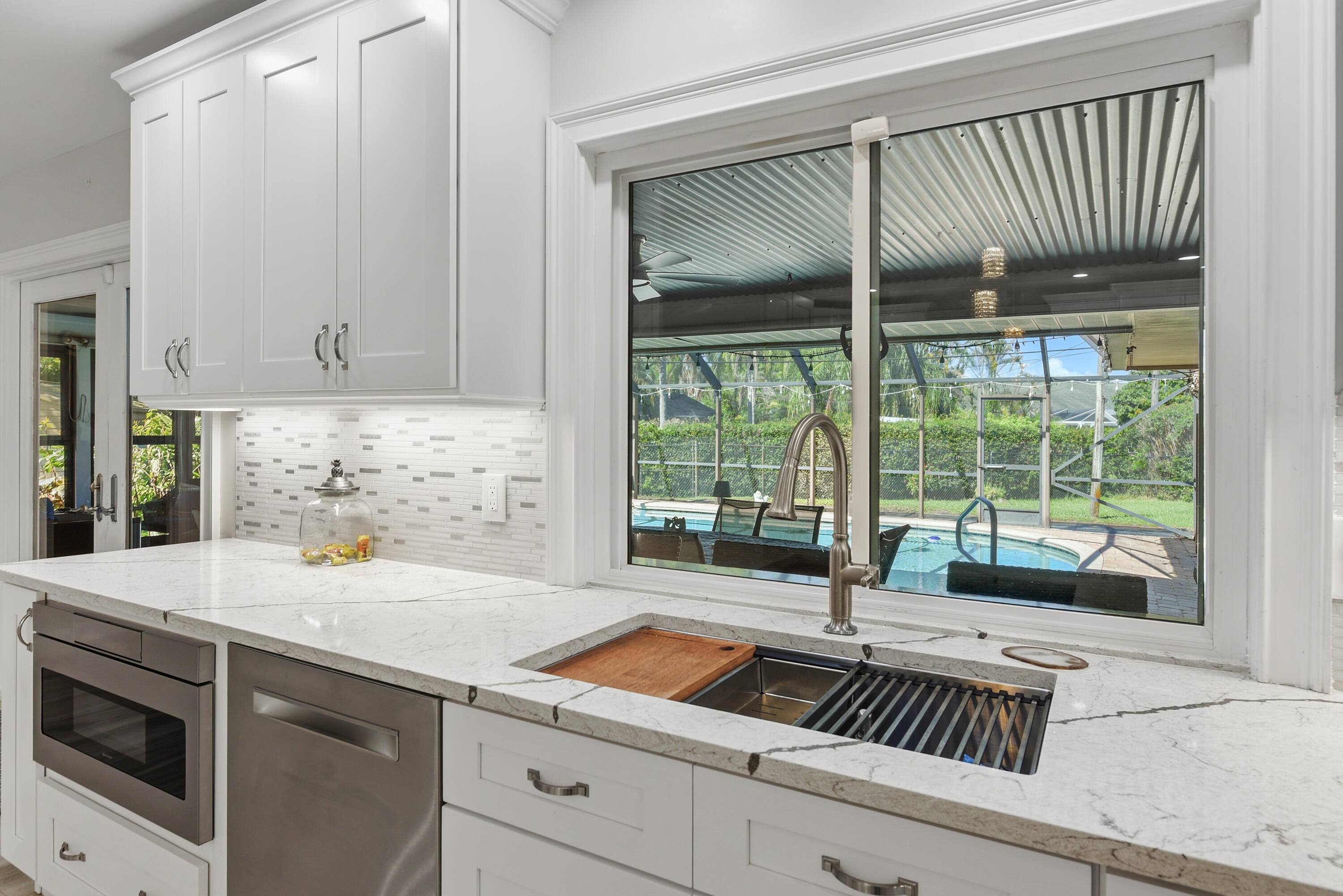 Enjoy picturesque pool views right from the kitchen! Features a double-basin stainless steel sink with built-in accessories, high-arc faucet, decorative tile backsplash, and beautiful marble-look countertops. A perfect blend of luxury and functionality!