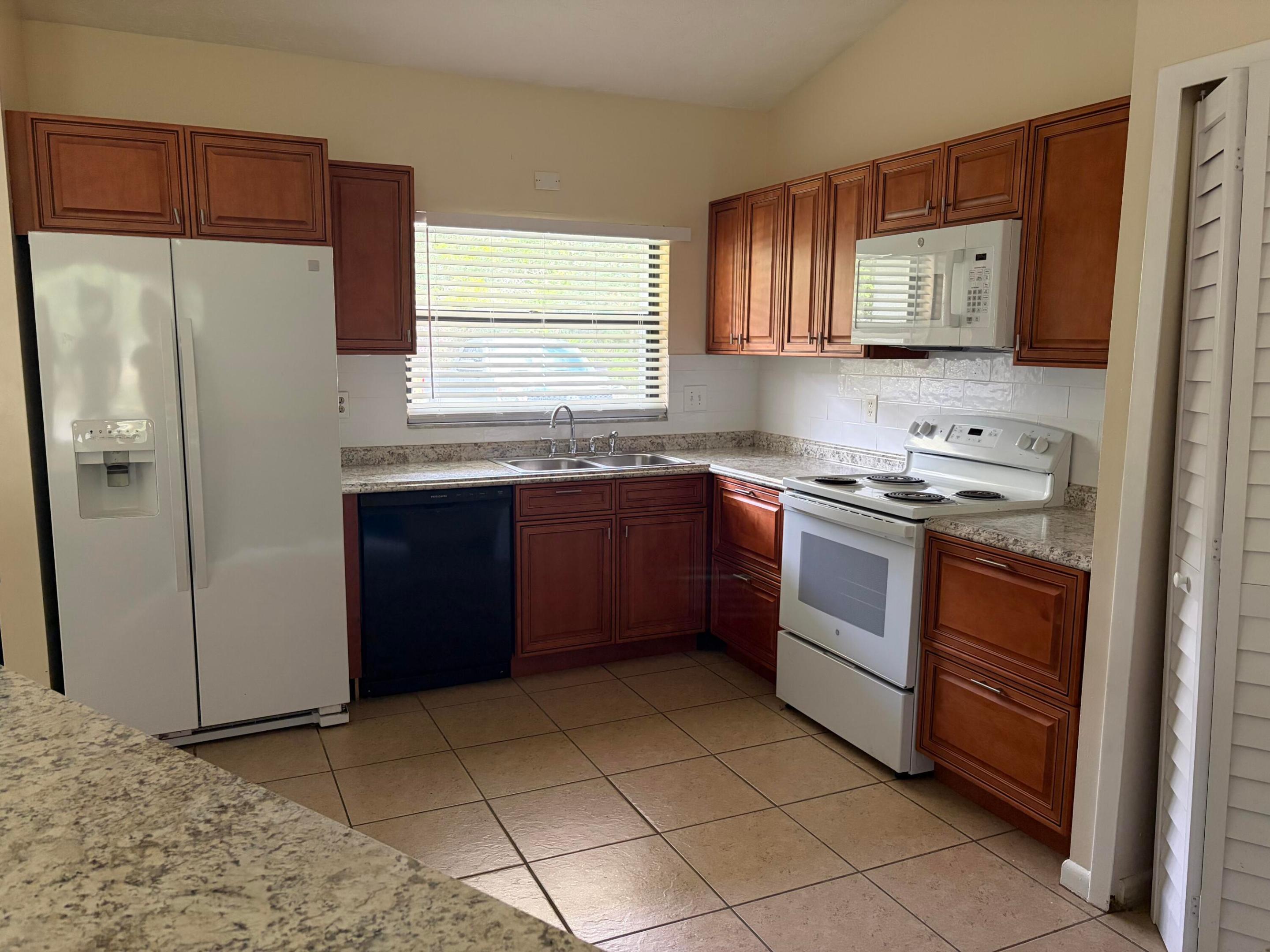 Kitchen featuring wood cabinetry, stone-finish countertops, tile flooring, and integrated white appliances Kitchen featuring wood cabinetry, stone-finish countertops, tile flooring, and integrated white appliances