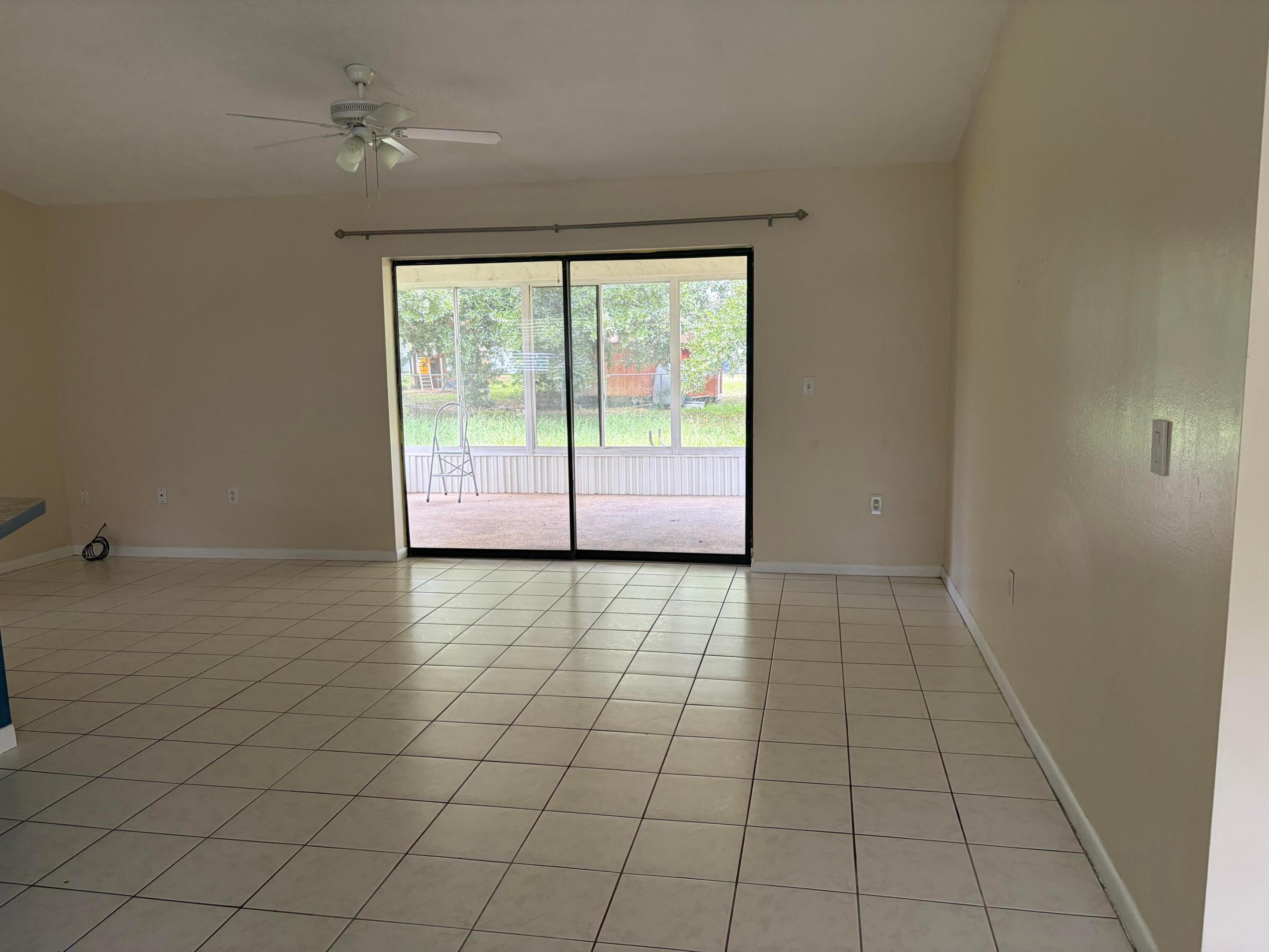 Spacious interior featuring neutral ceramic tile flooring, a central ceiling fan with integrated lighting, and sliding glass doors that open to an enclosed patio Spacious interior featuring neutral ceramic tile flooring, a central ceiling fan with integrated lighting, and sliding glass doors that open to an enclosed patio