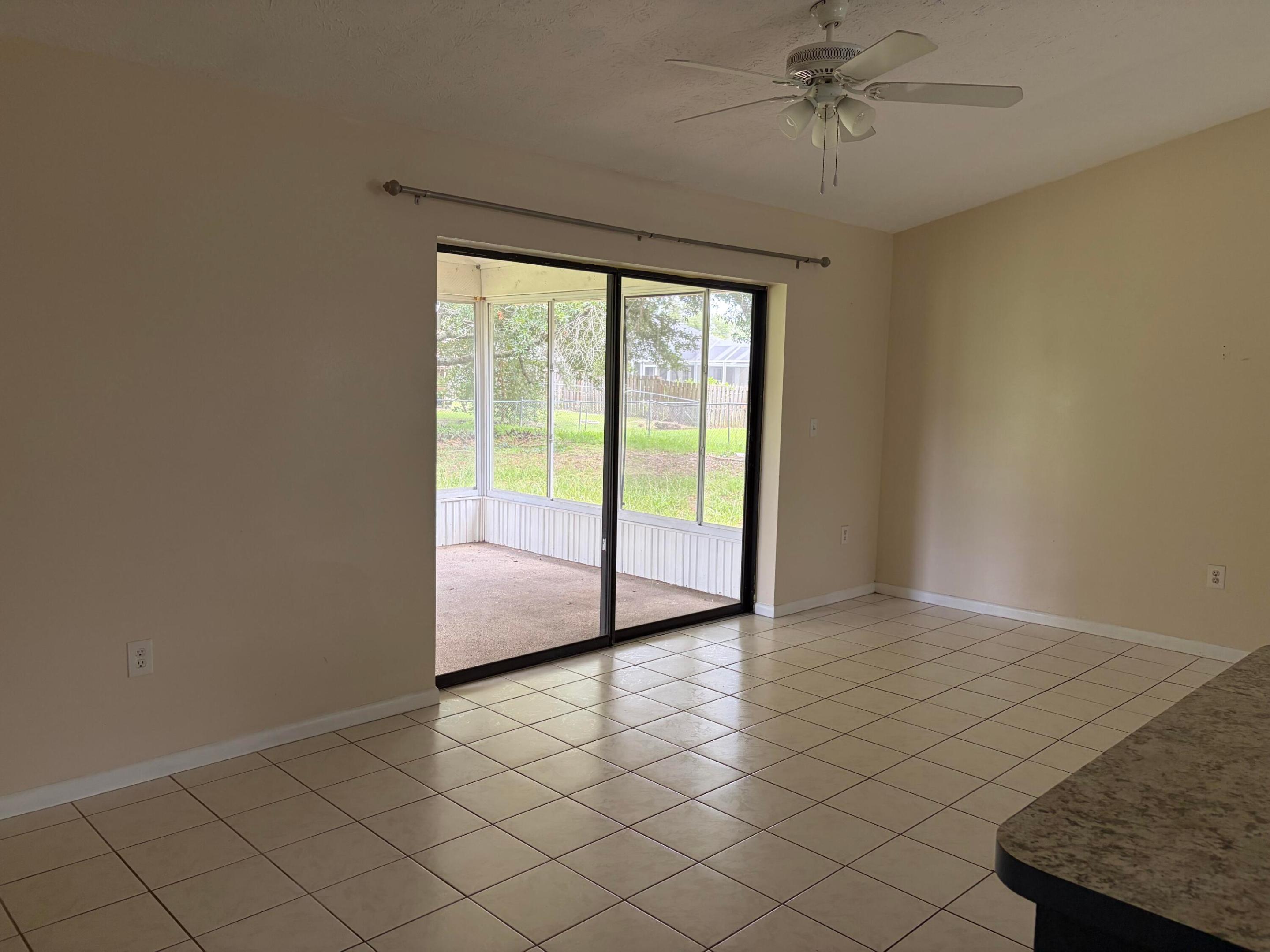 Ceramic tile flooring, vaulted ceiling with a white overhead fan, and sliding glass doors opening to a screened-in lanai Ceramic tile flooring, vaulted ceiling with a white overhead fan, and sliding glass doors opening to a screened-in lanai