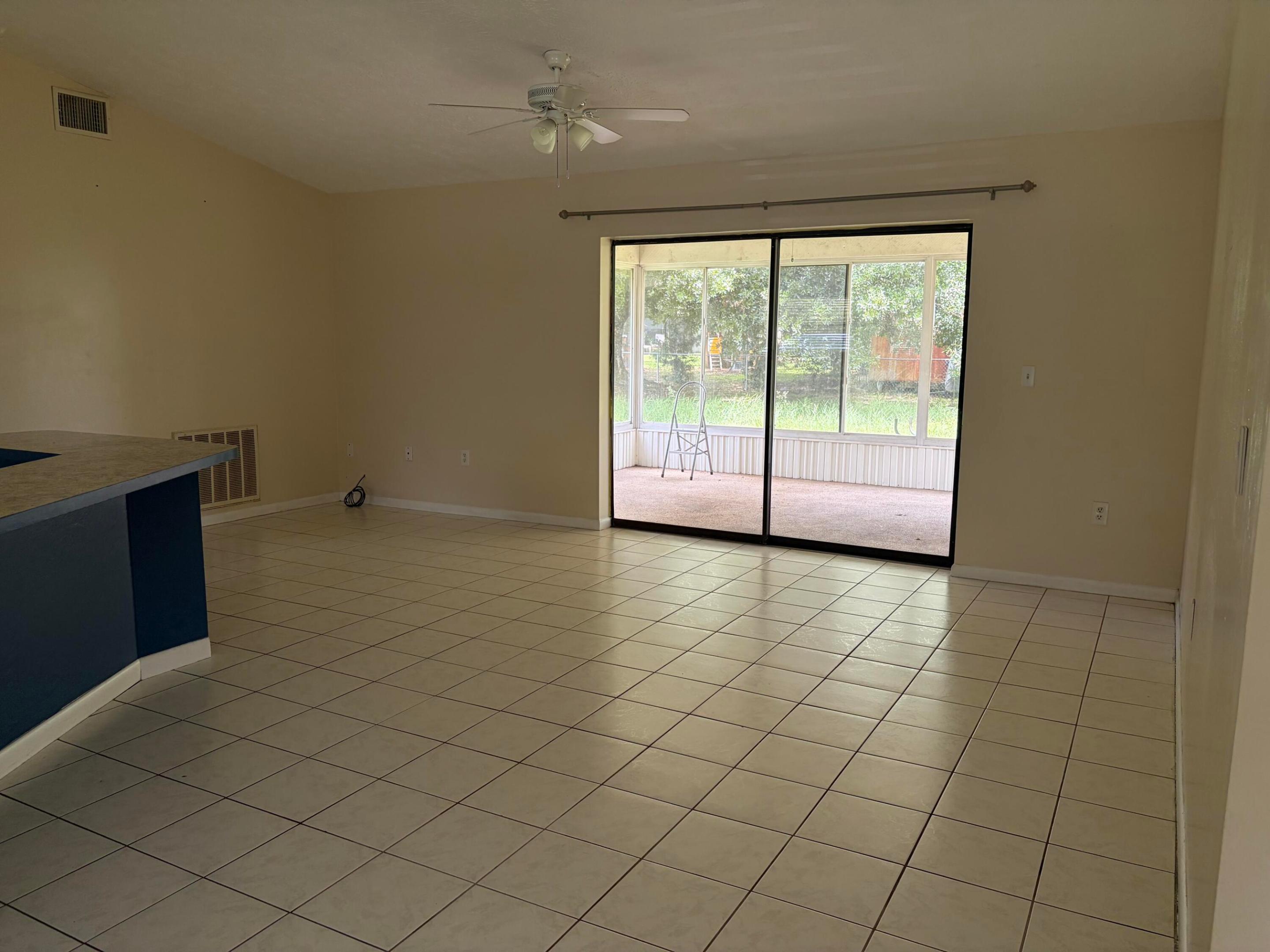 Open floor plan featuring tile flooring, ceiling fan, and sliding glass doors leading to a screened porch area Open floor plan featuring tile flooring, ceiling fan, and sliding glass doors leading to a screened porch area