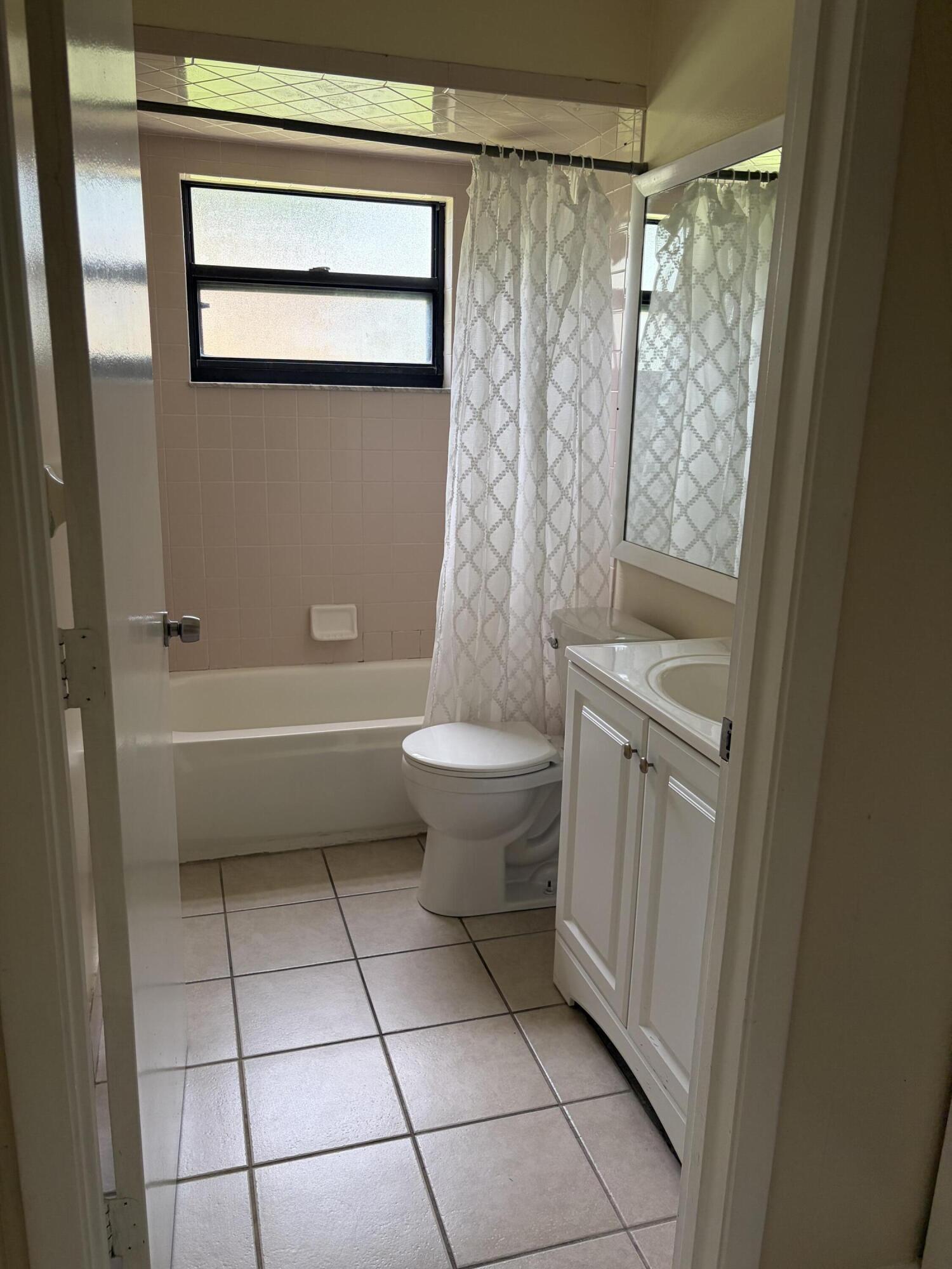 Bathroom featuring a white vanity cabinet with a integrated sink, ceramic tile flooring, a bathtub with wall-mounted soap dish, and a framed mirror