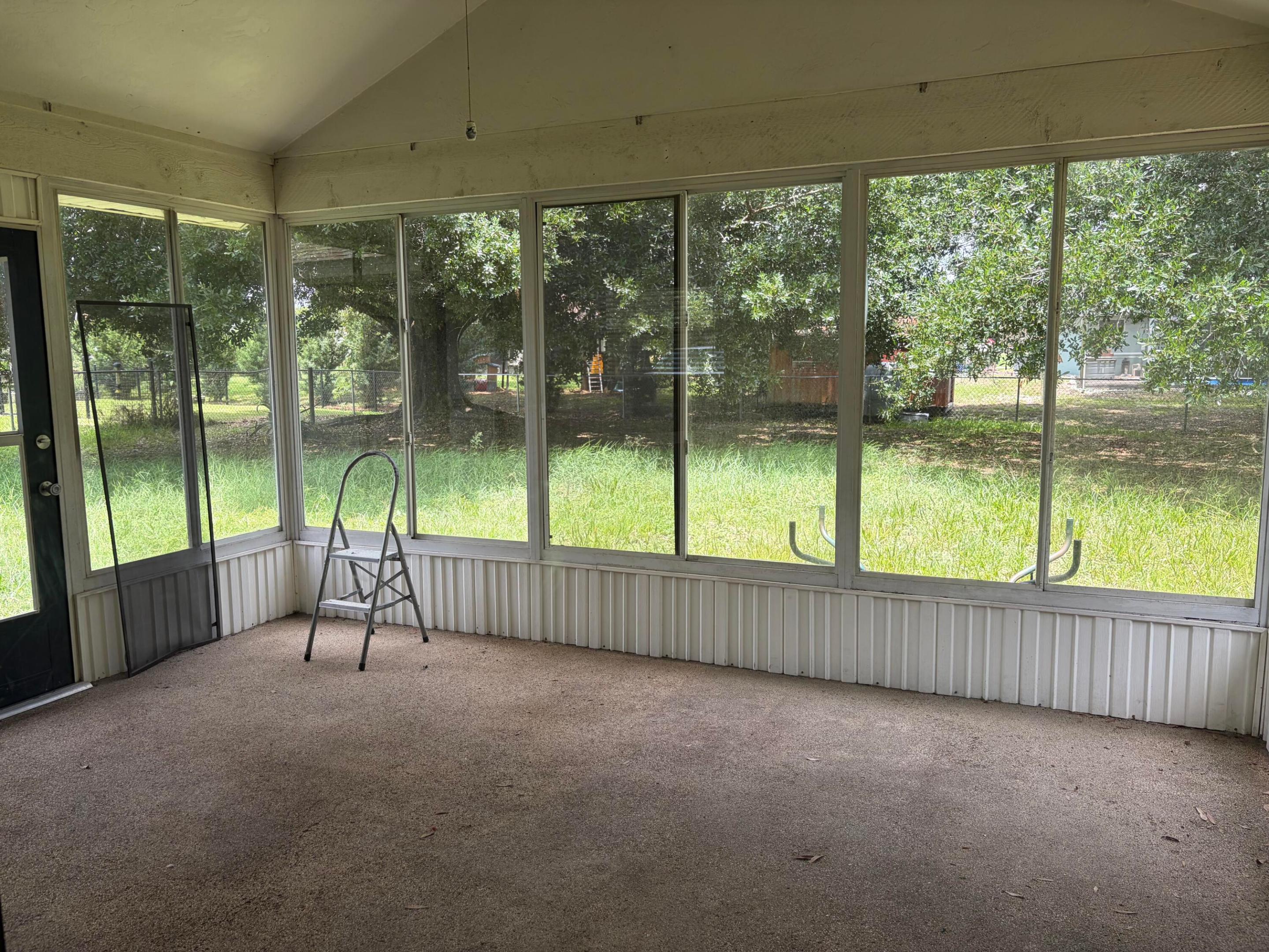 Enclosed sunroom featuring expansive glass wall panels, a vaulted ceiling, and exterior yard access