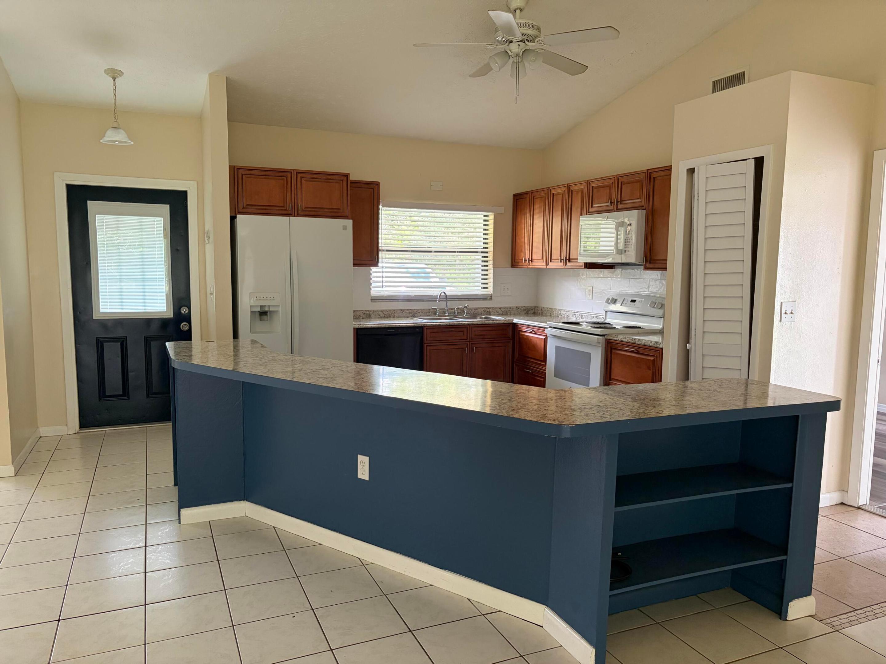 Kitchen featuring wood cabinetry, solid-surface countertops, built-in shelving, vaulted ceiling, and ceramic tile flooring Kitchen featuring wood cabinetry, solid-surface countertops, built-in shelving, vaulted ceiling, and ceramic tile flooring