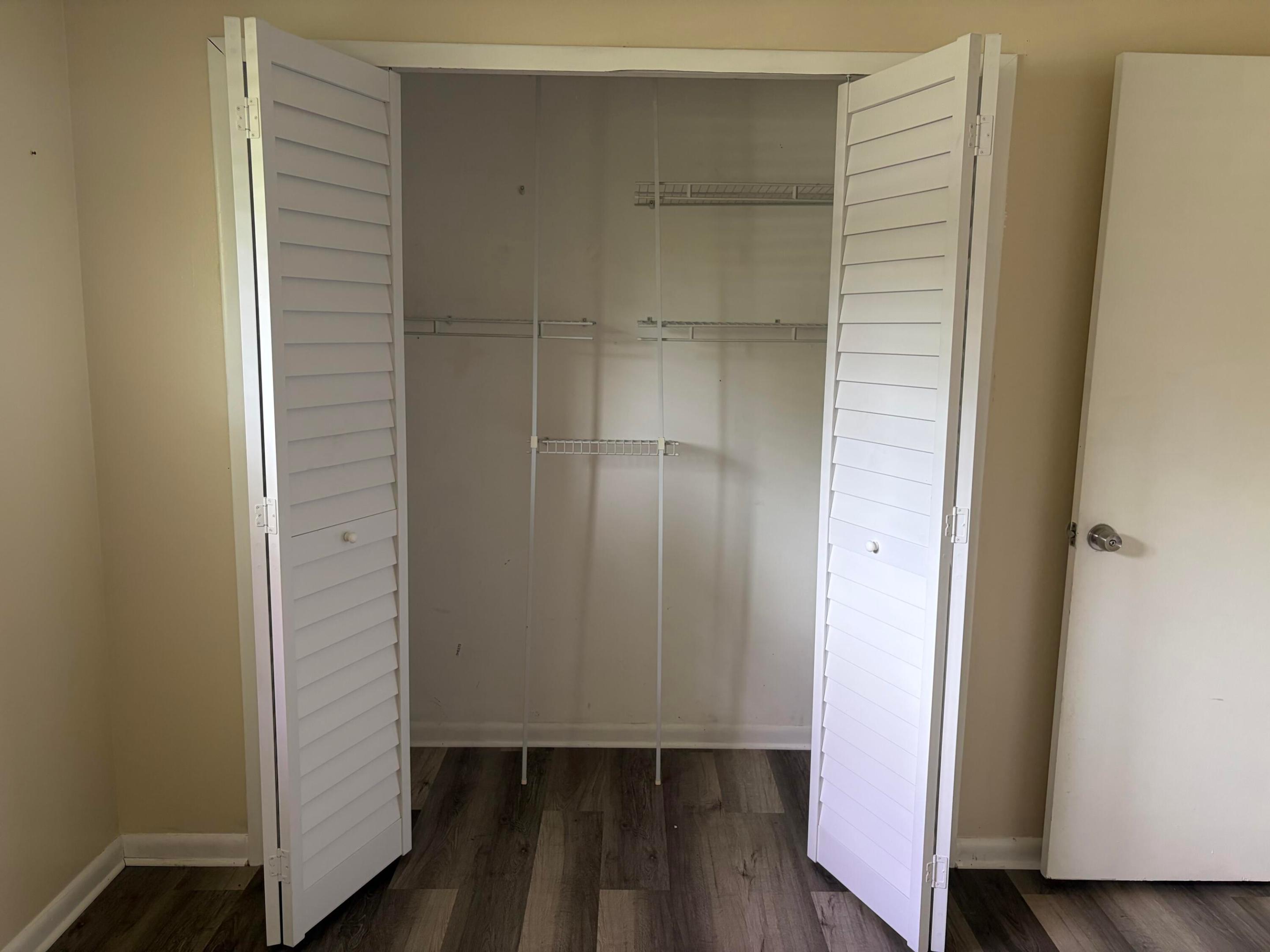 Reach-in closet featuring white louvered bi-fold doors, white wire shelving, and wood-finish flooring