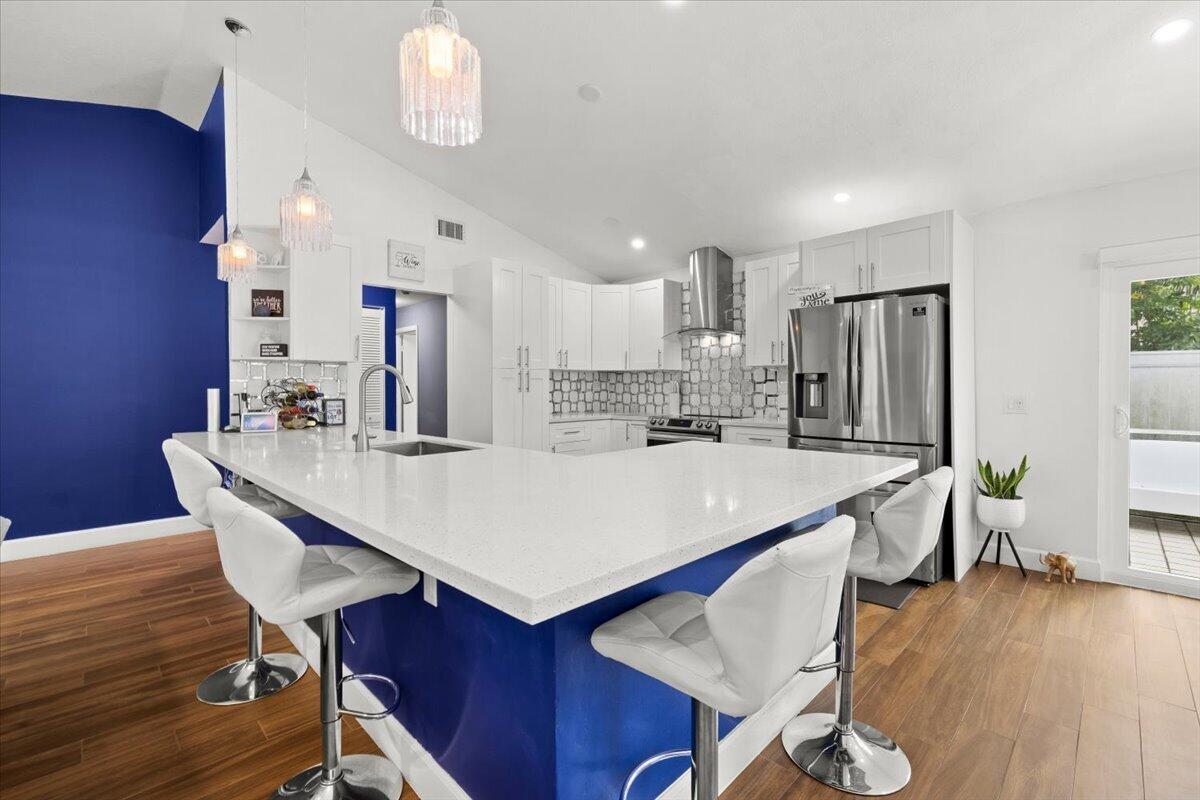Kitchen featuring white shaker-style cabinetry, quartz countertops, geometric tile backsplash, stainless steel range hood, and wood-finish flooring