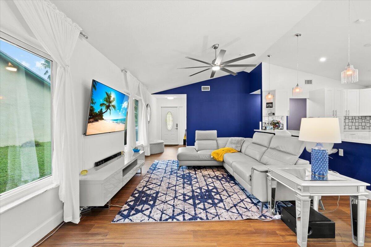 Vaulted ceilings with a ceiling fan, wood-finish flooring, accent wall, and natural light from large windows