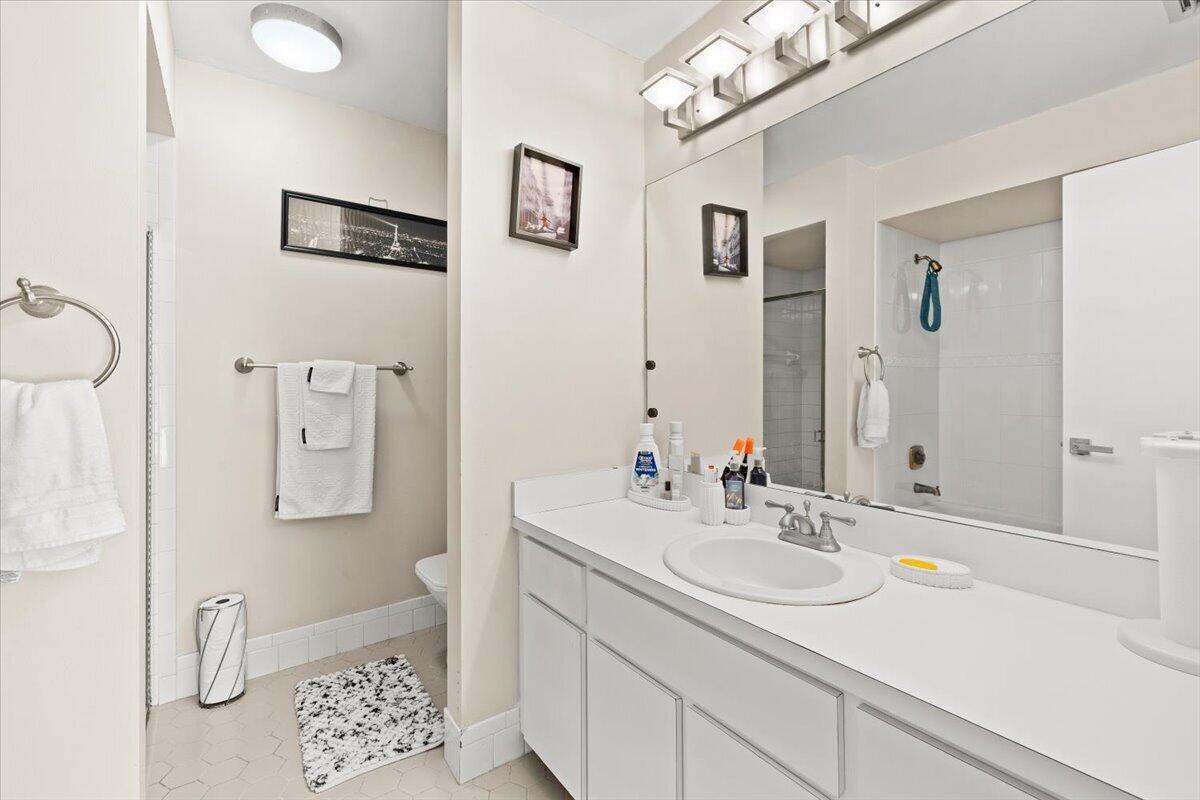 Bathroom featuring a vanity with a white countertop and oval under-mount sink, full-width wall mirror, four-light vanity fixture, and a tub-shower combination with white wall tile