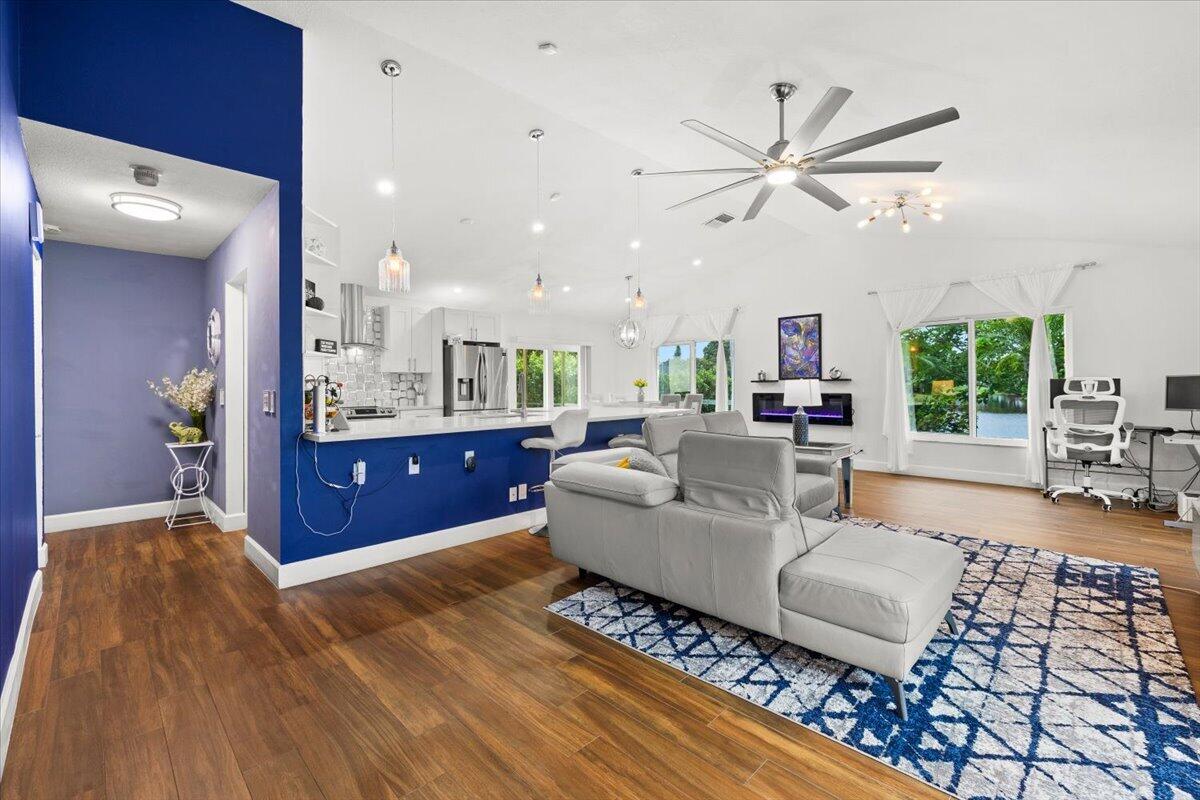 Open-concept room featuring wood-finish flooring, vaulted ceilings with an oversized ceiling fan, wall-mounted electric fireplace, and a kitchen island with pendant lighting