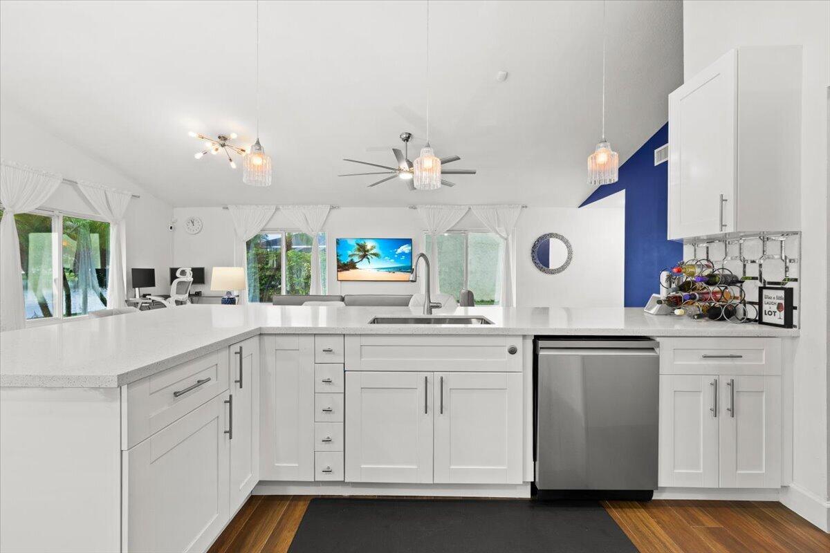 Kitchen featuring white cabinetry, quartz countertops, stainless steel dishwasher, wood-finish flooring, and multi-pendant lighting