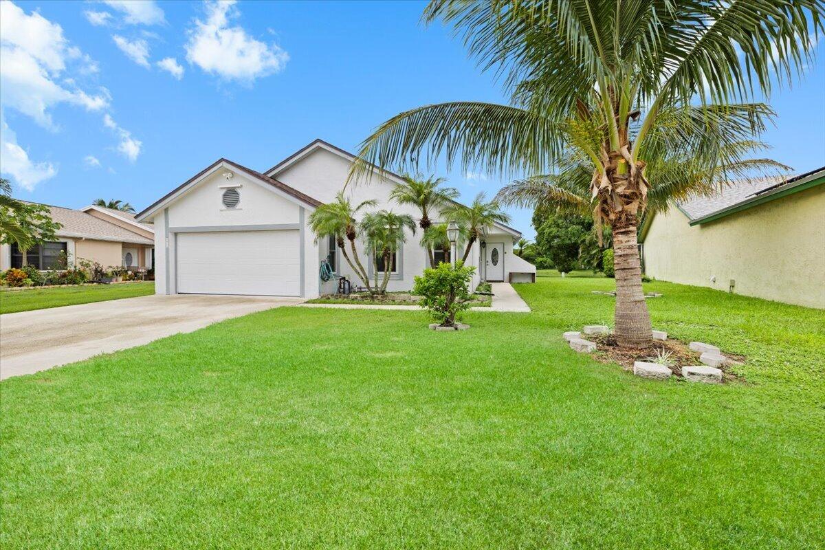 Stucco exterior residence featuring an attached two-car garage, pitched roofline, concrete driveway, and landscaped front yard with palm trees Stucco exterior residence featuring an attached two-car garage, pitched roofline, concrete driveway, and landscaped front yard with palm trees