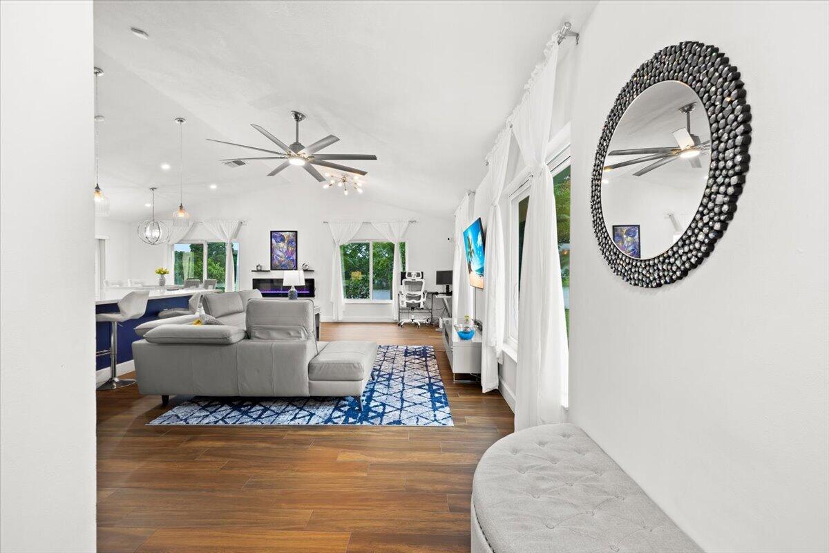 Vaulted ceiling featuring a multi-blade ceiling fan, wide-plank wood-finish flooring, built-in electric fireplace, and multiple windows
