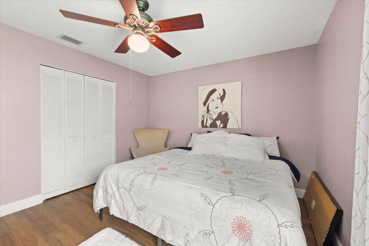 Room featuring wood-finish flooring, a ceiling fan with integrated lighting, and white louvered-panel closet doors