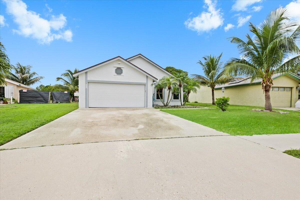Single-story residence featuring a concrete driveway, two-car garage, stucco exterior, and landscaped lawn with mature palm trees
