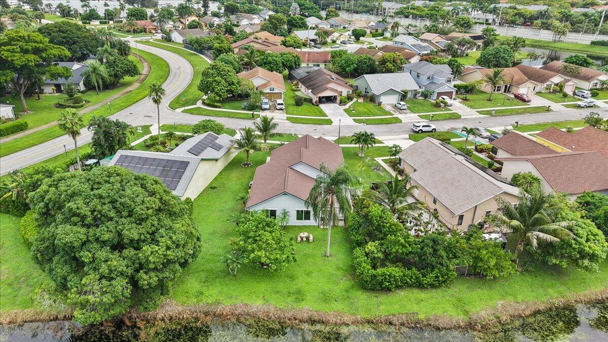 Aerial perspective of a property featuring roof-mounted solar panels, a sprawling lawn, mature landscaping, and waterfront grounds