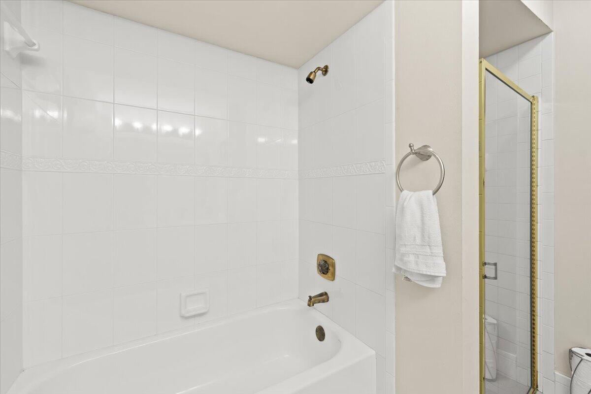 Full-height white wall tile, built-in recessed soap dish, metallic shower and tub fixtures, and a separate glass-enclosed shower stall with a gold-tone frame