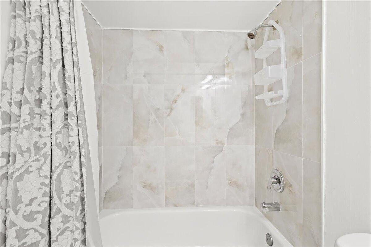 Bathtub alcove featuring full-height stone-finish wall tile, a single-handle chrome shower faucet, and a wall-mounted chrome tub spout