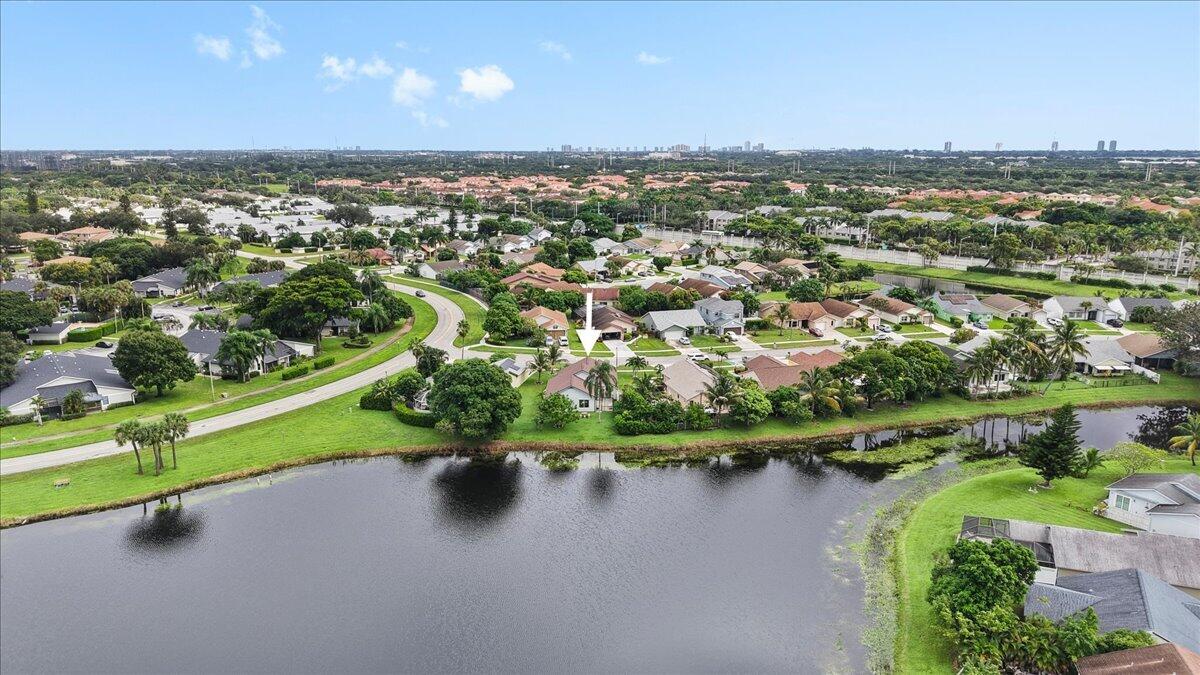 Aerial perspective featuring a waterfront lot, expansive green space, and mature landscaping within a suburban community