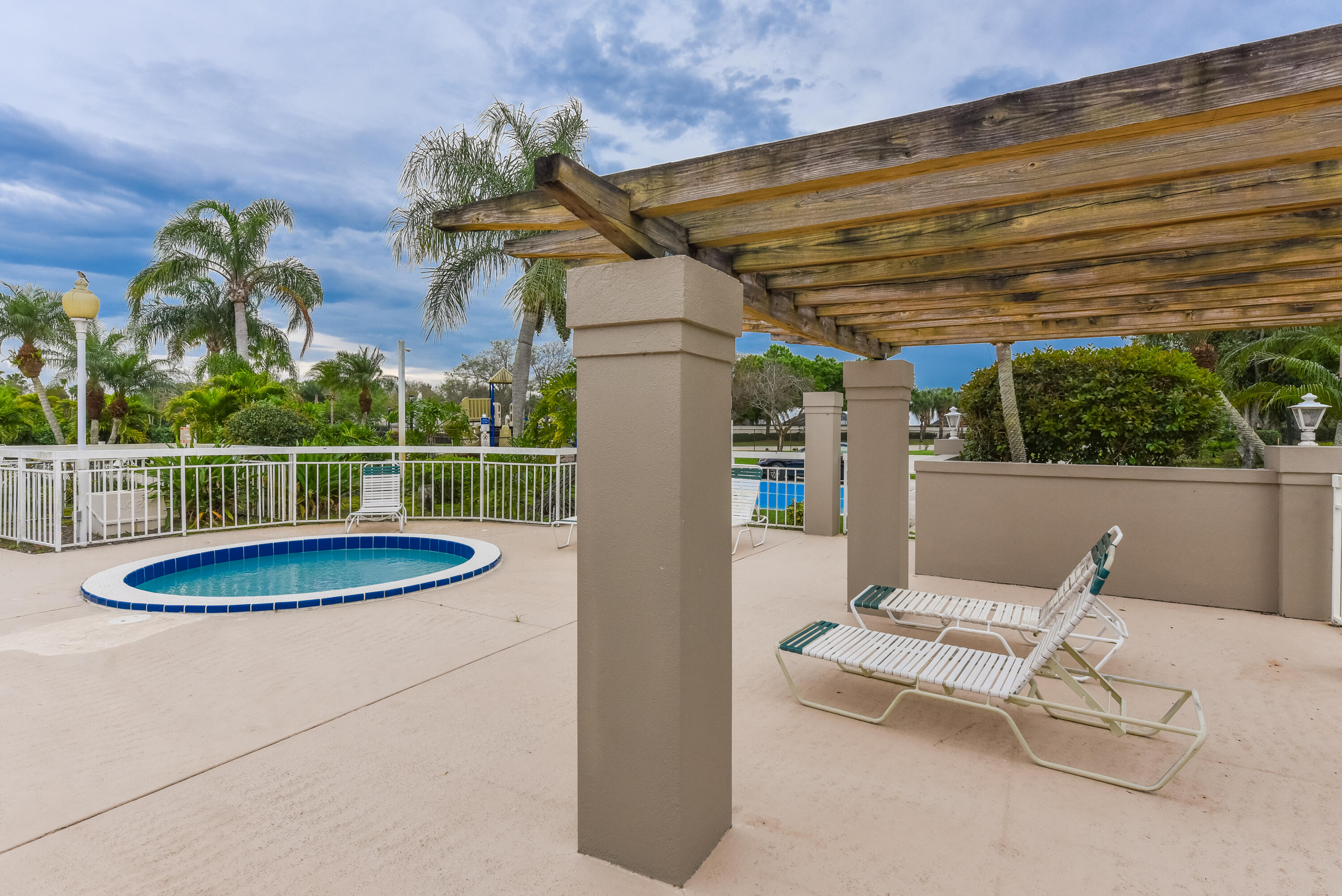 Outdoor terrace featuring a wood-beam pergola, concrete decking, built-in pool, and white metal fencing