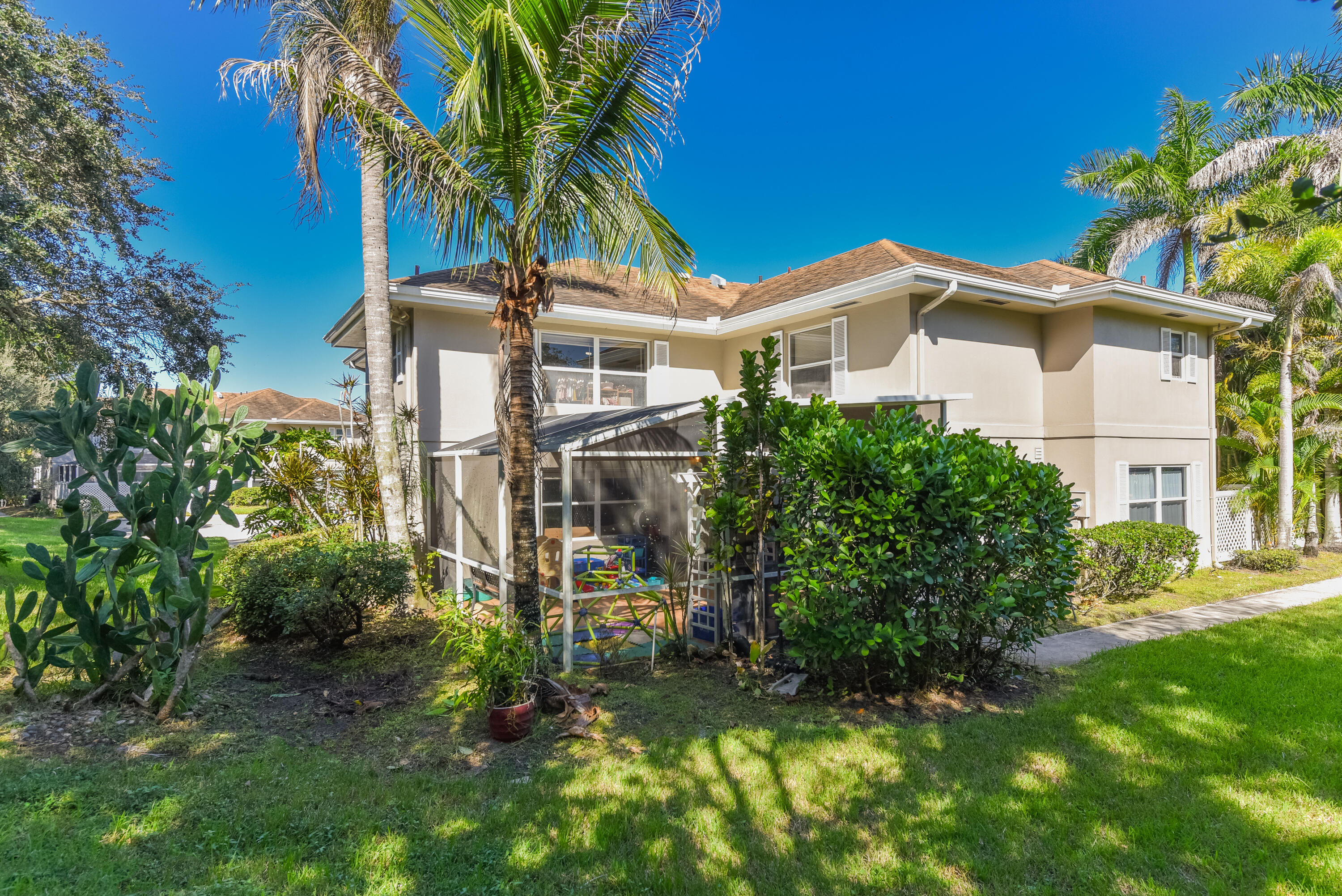Two-story exterior featuring a screened-in lanai, stucco siding, a shingled hip roof, and lush landscaping