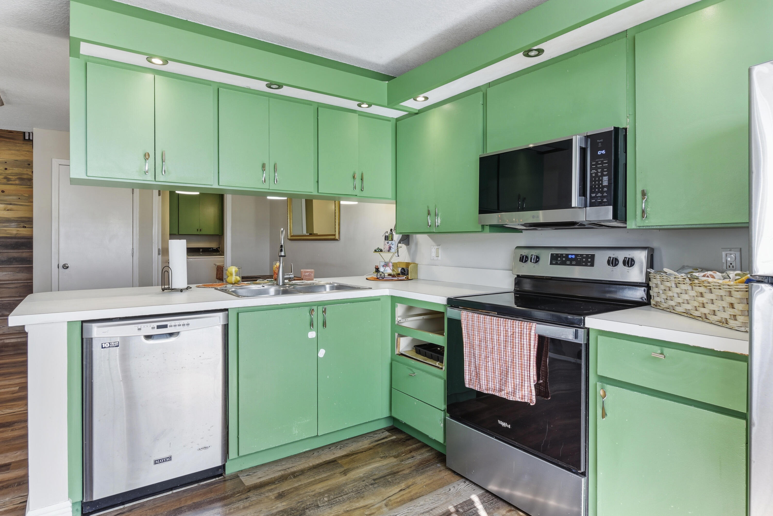 Kitchen featuring flat-panel cabinetry, stainless steel appliances, white solid-surface countertops, dual-basin sink, and recessed lighting