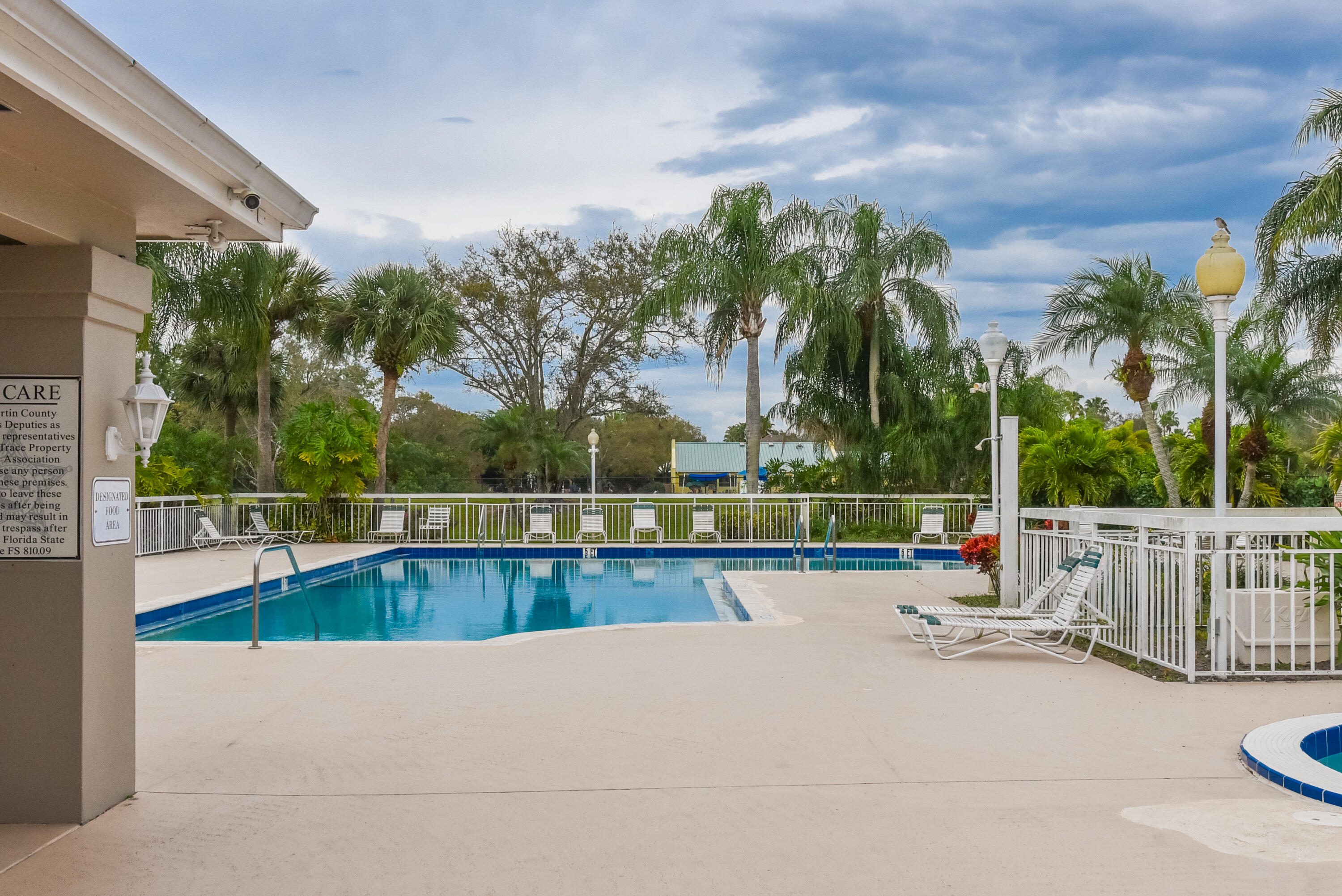 Swimming pool with surrounding concrete deck, perimeter fencing, and exterior pole lighting
