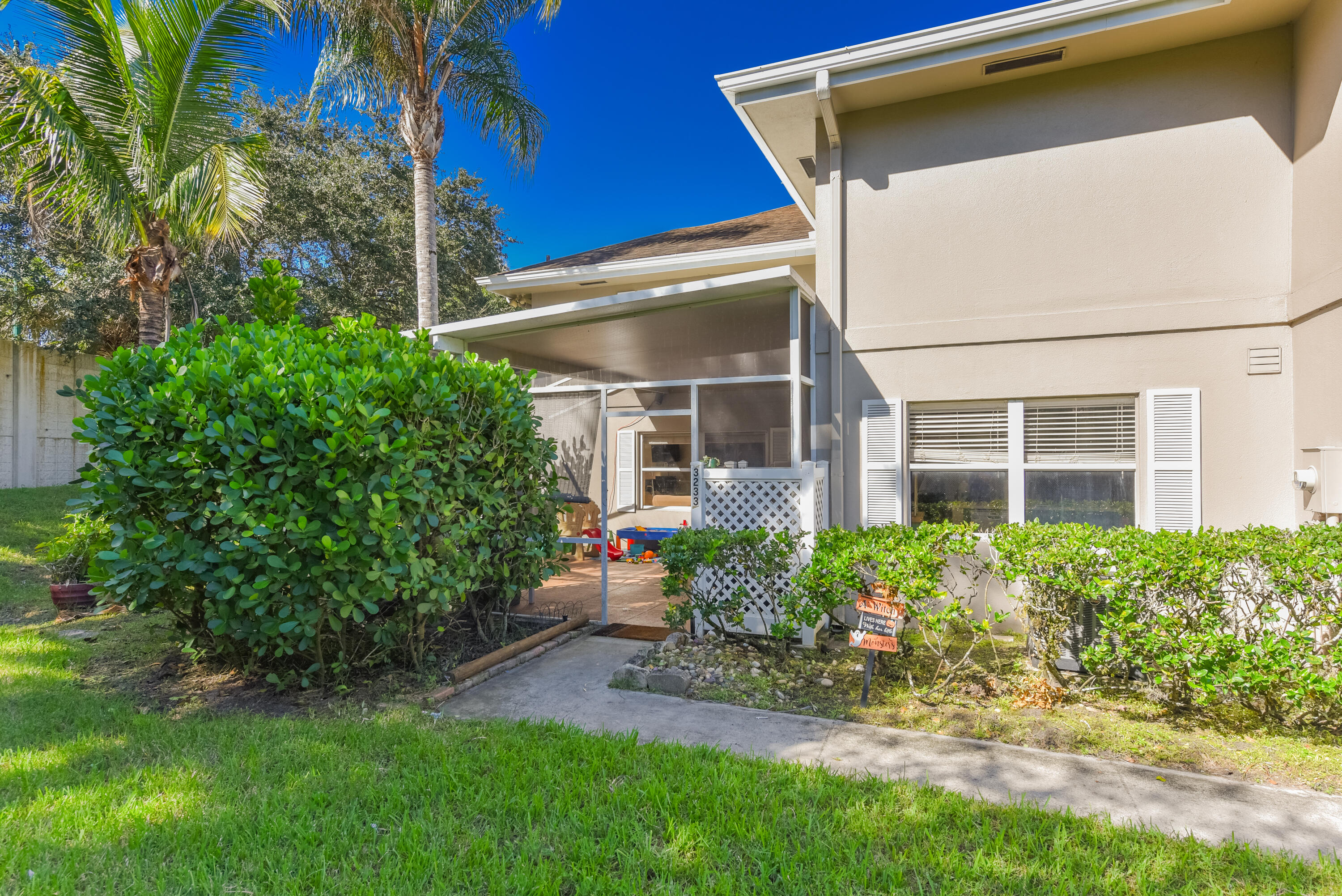 Exterior featuring a screened-in lanai, concrete walkway, and manicured landscaping including mature palm trees