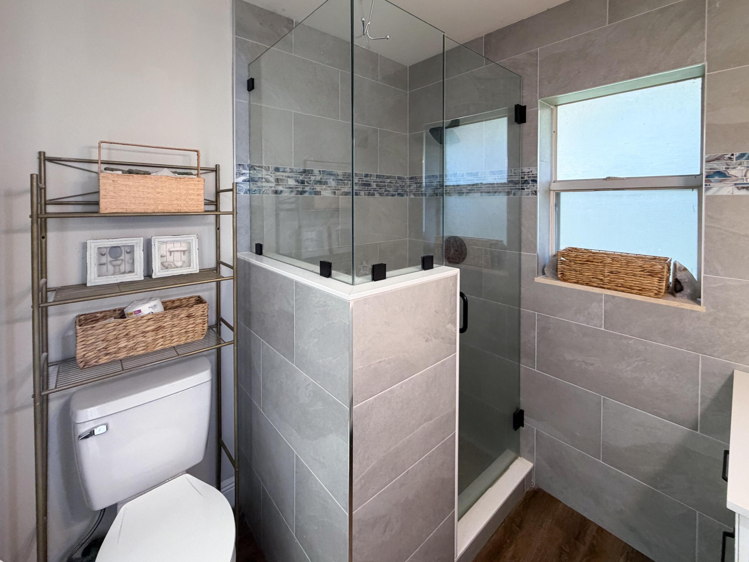 Walk-in shower featuring glass enclosure, gray tile surround with decorative mosaic accent strip, and wood-finish flooring