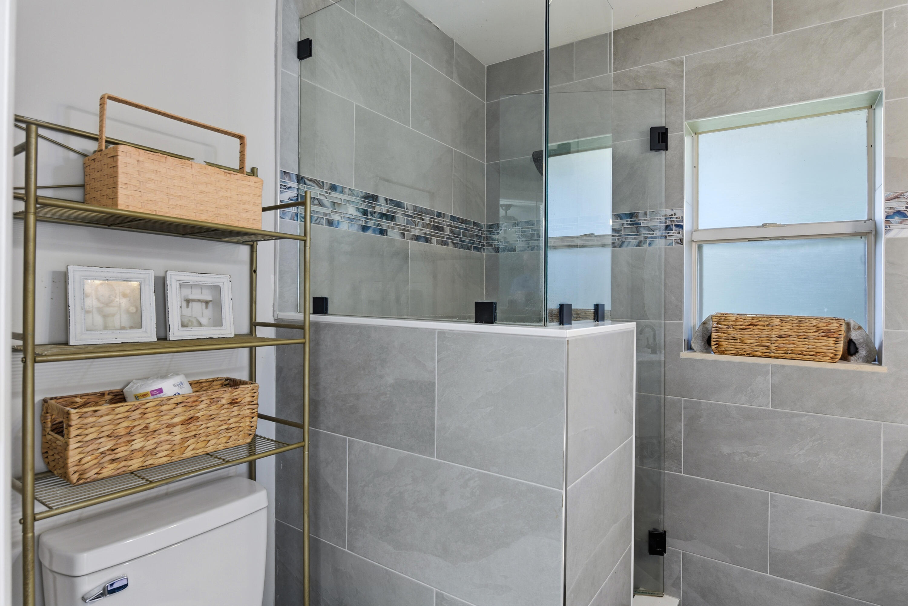 Walk-in shower featuring large-format grey tile, a glass enclosure, decorative mosaic tile accents, and a window
