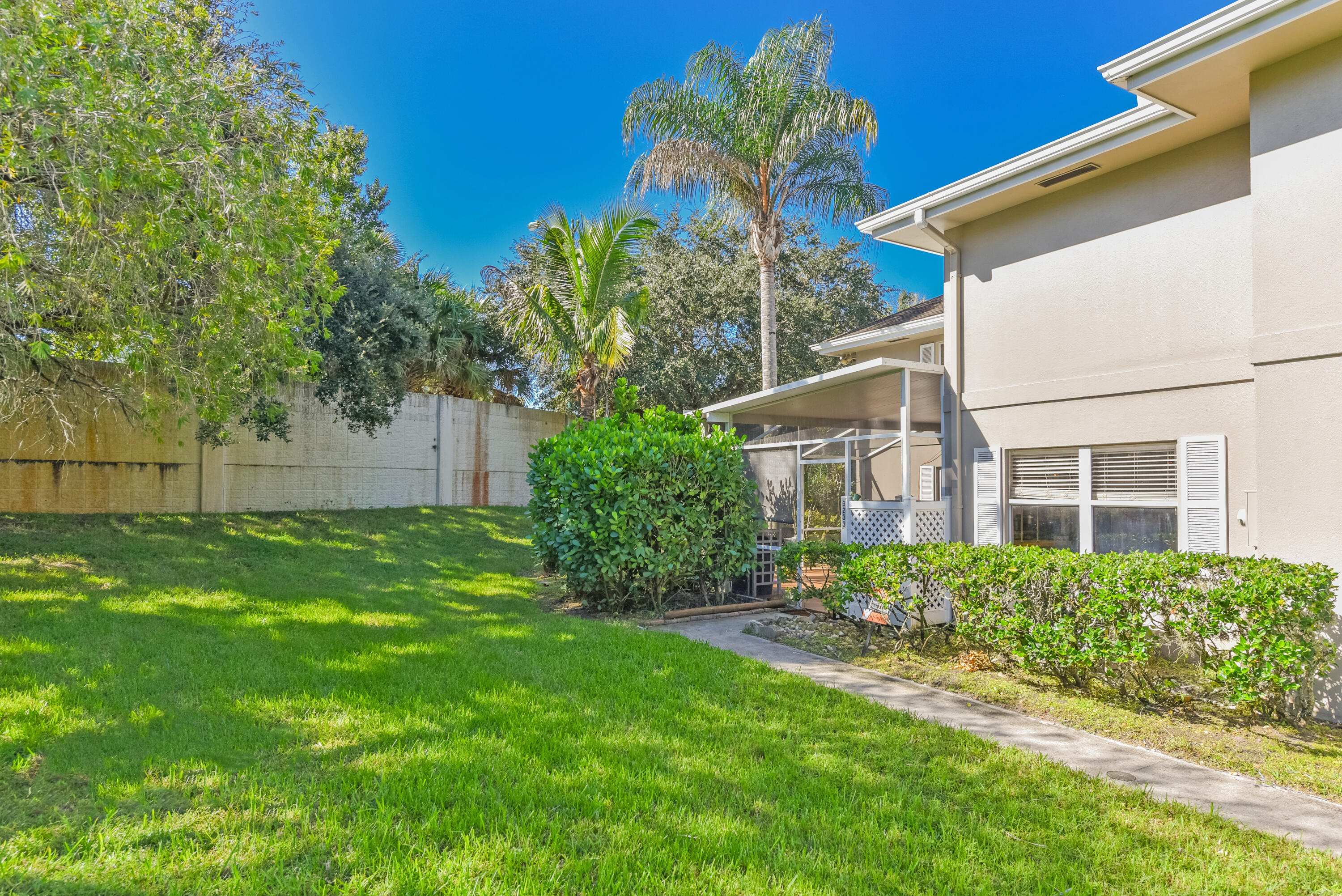 Backyard featuring a manicured lawn, concrete walkway, screened-in porch, and perimeter wall