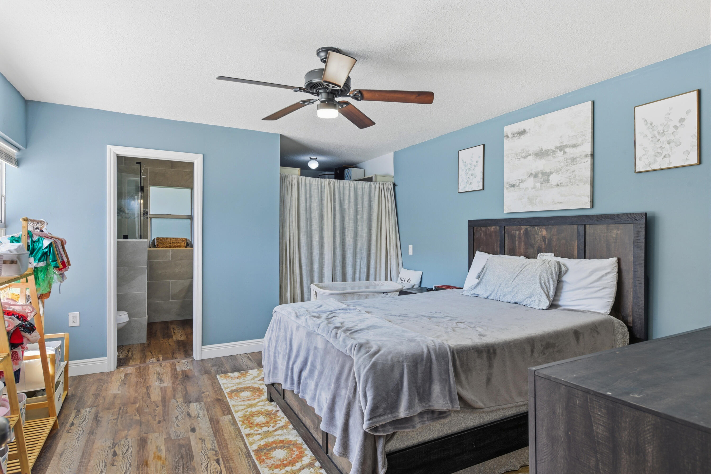 Bedroom featuring wood-finish flooring, a multi-blade ceiling fan with integrated lighting, and a doorway entry to a tiled bathroom