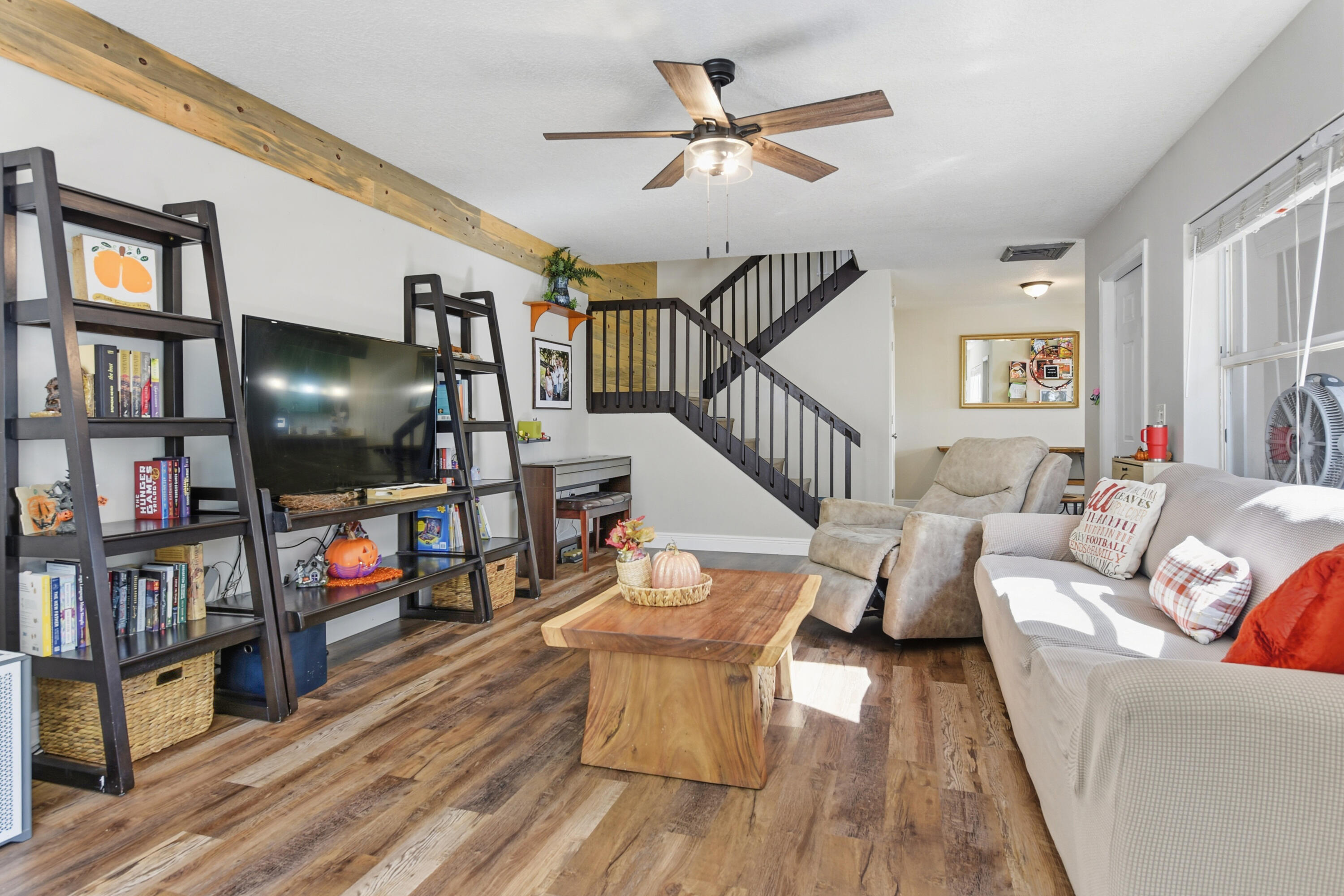 Living area featuring wood-finish flooring, exposed timber ceiling beam, and a staircase with a dark-finish wood railing