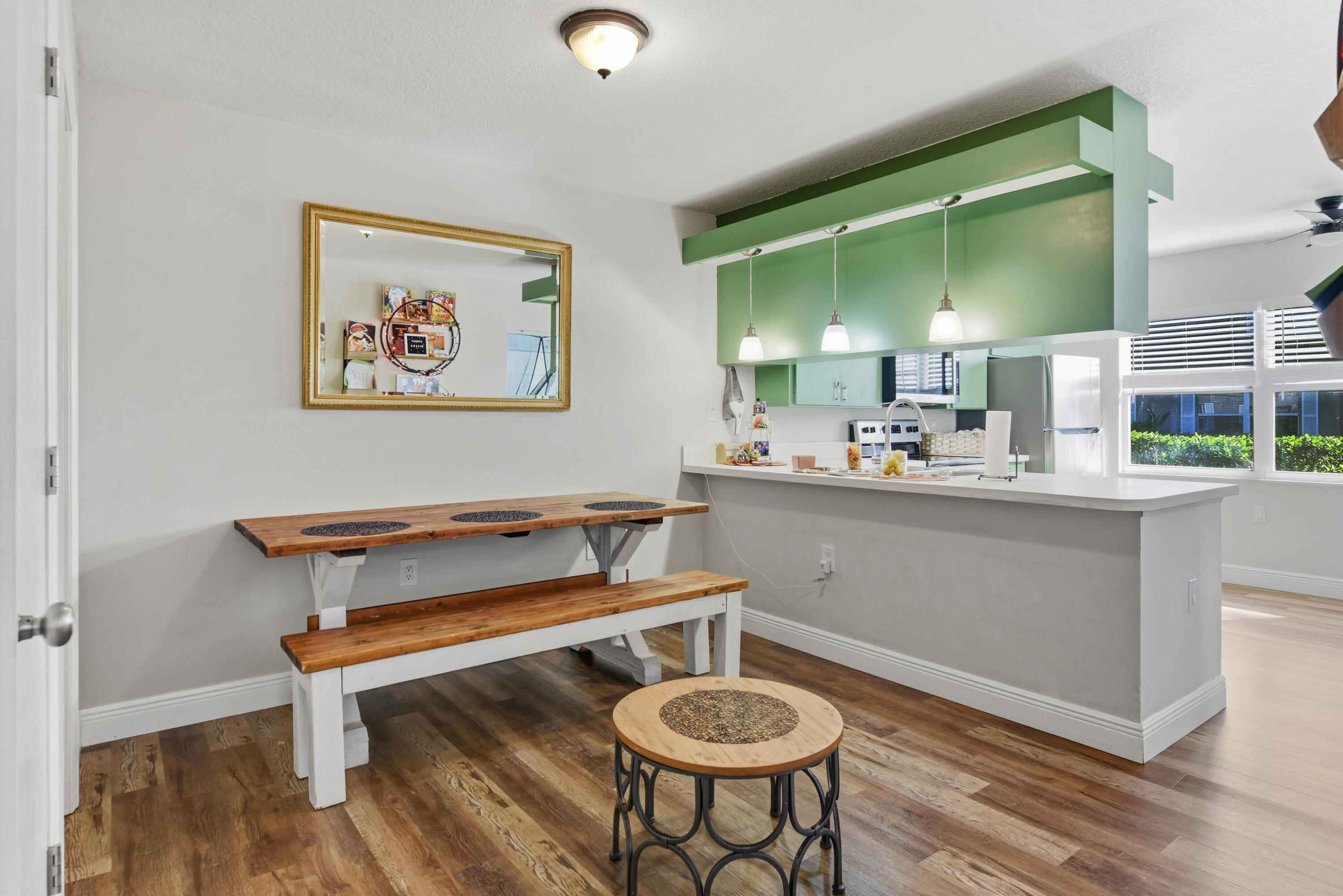 Kitchen area featuring a peninsula with a solid surface countertop, pendant lighting, custom green-painted soffit cabinetry, and wood-finish flooring